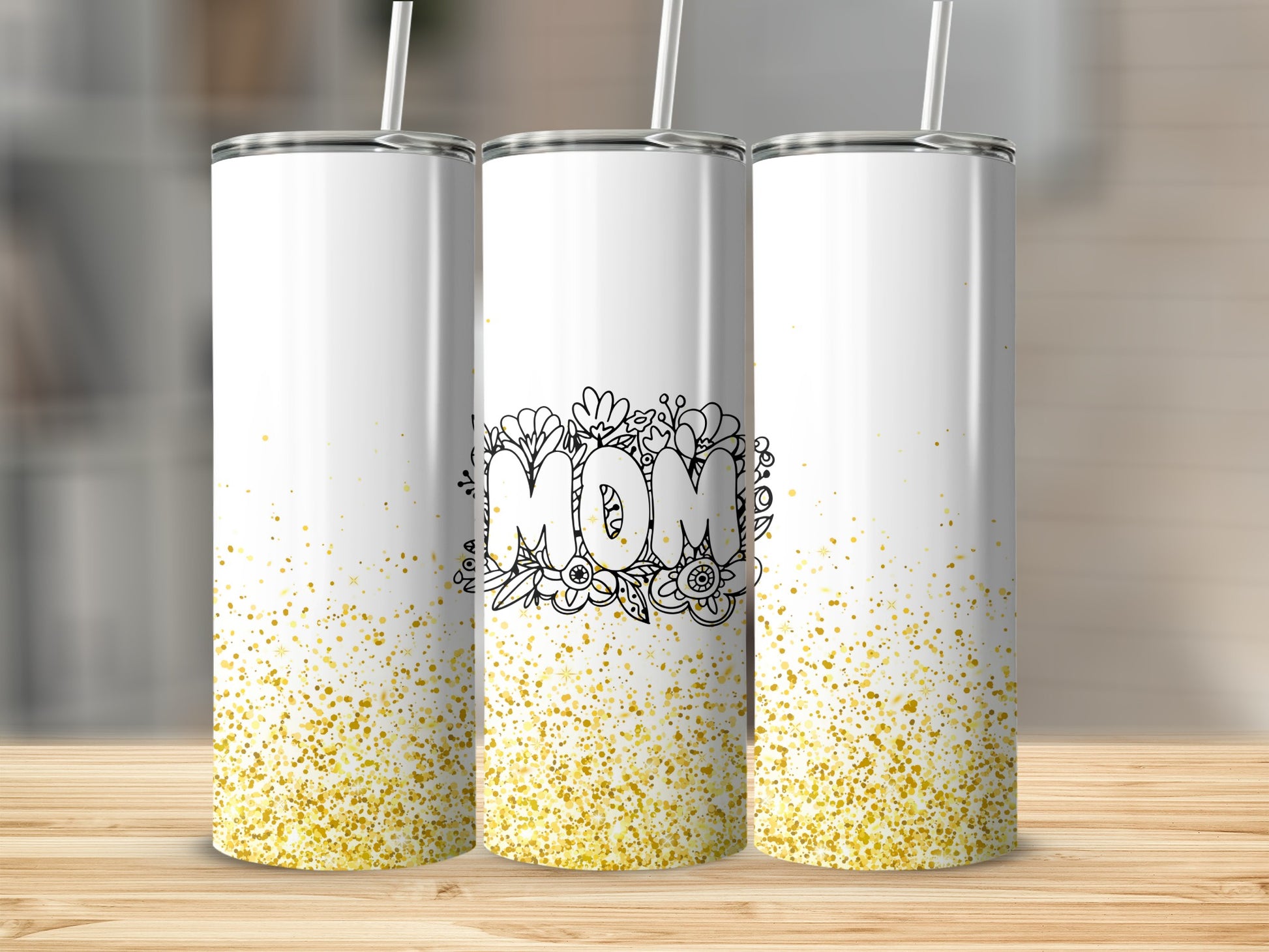 Three white tumblers with "Mom" in floral lettering and gold glitter.