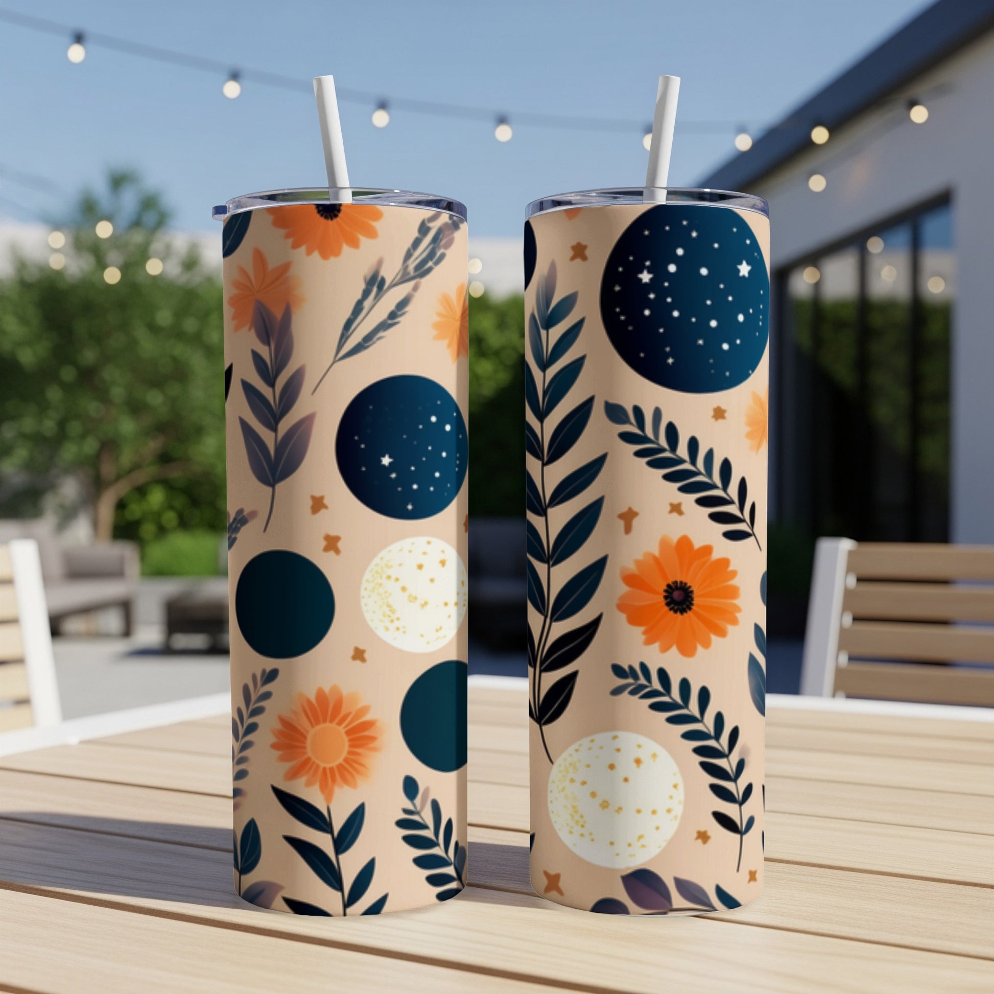 Two tall tumblers with celestial and floral patterns on an outdoor table.