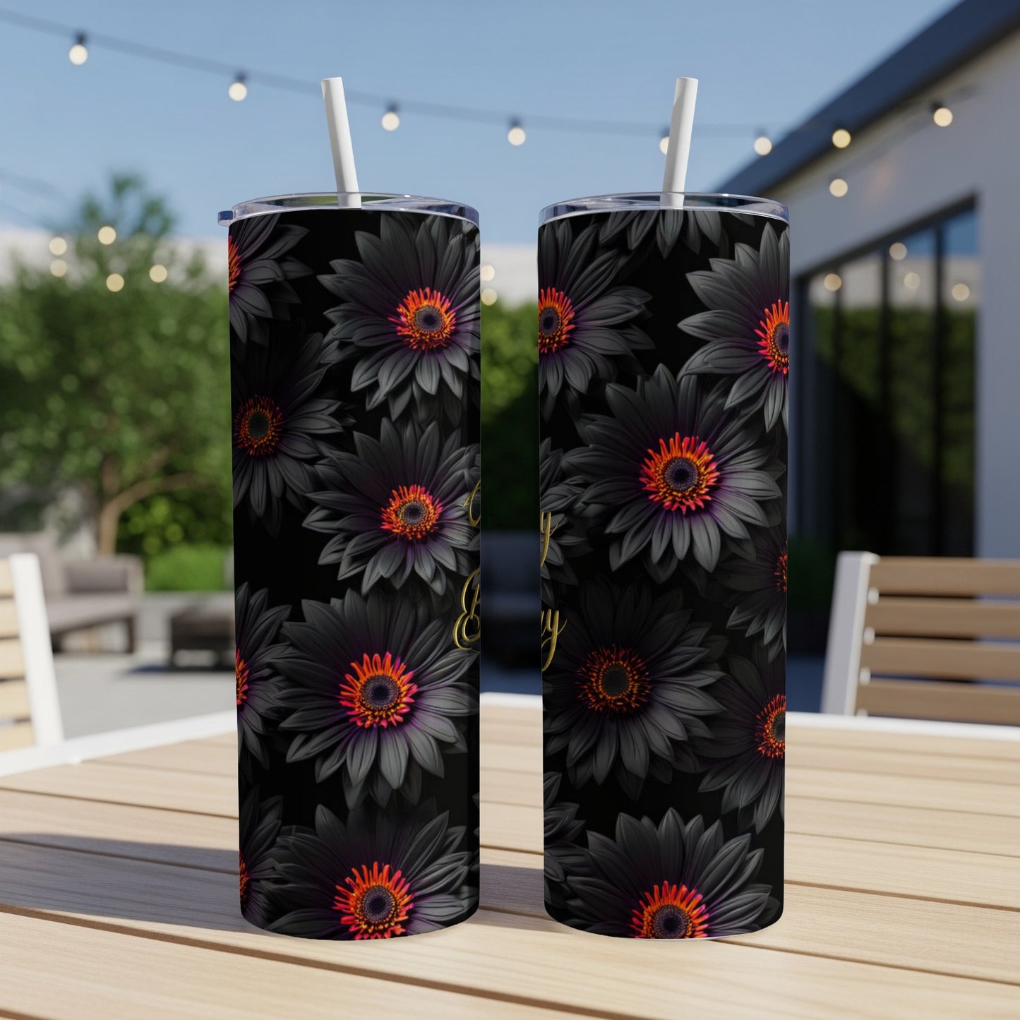 Black floral tumbler with straw on outdoor table.