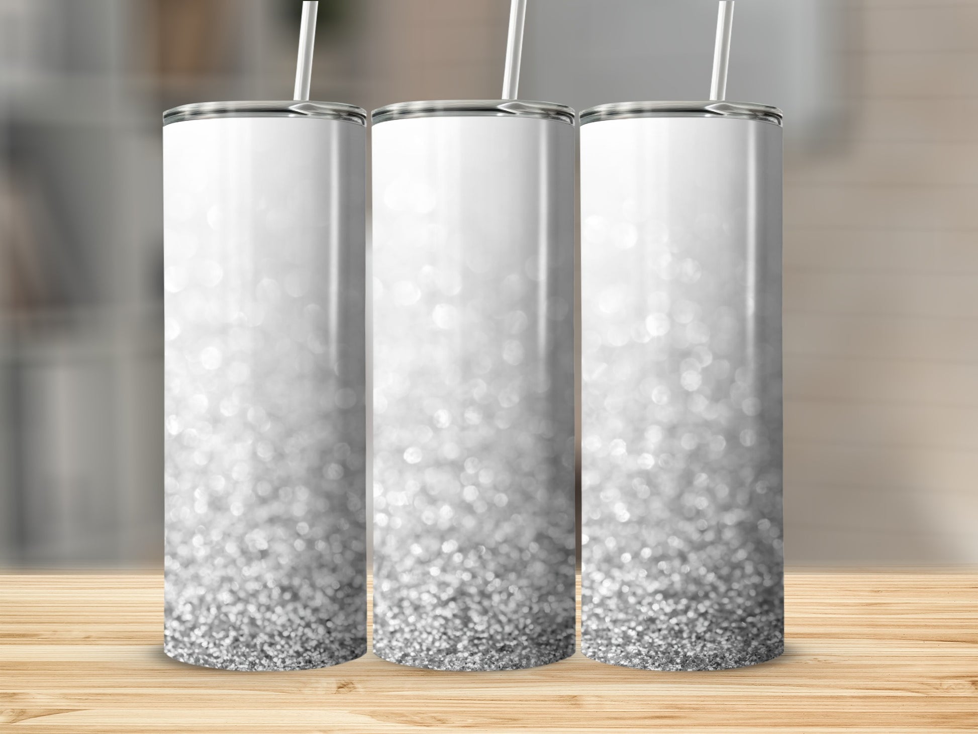 Three silver glitter tumblers with straws on a wooden surface.