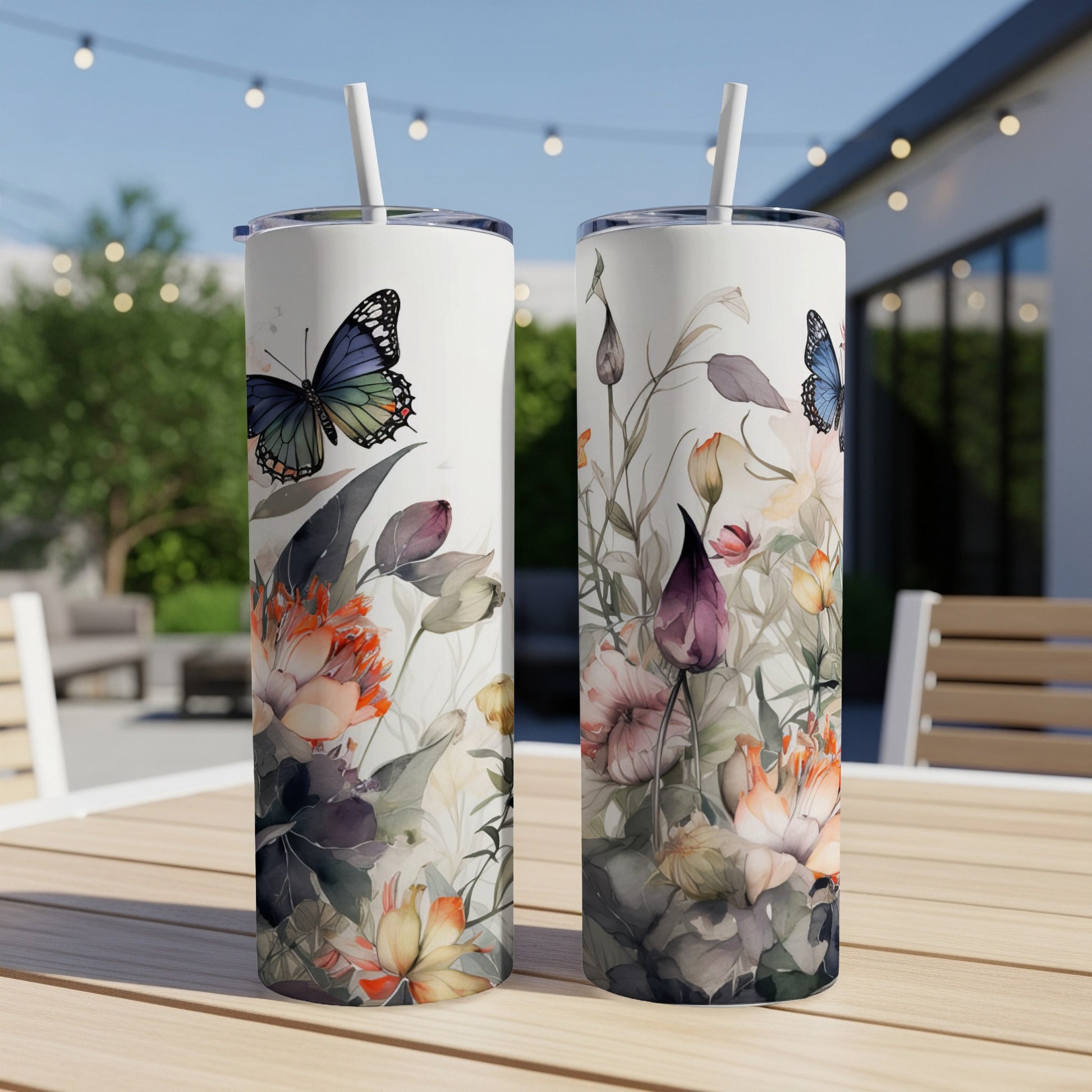 Two tumblers with floral and butterfly watercolor design on outdoor patio table.