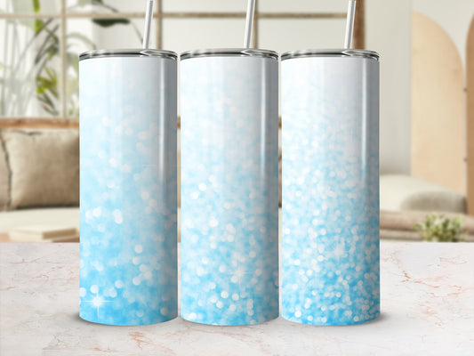 Three blue glitter ombre tumblers with straws on a marble countertop.