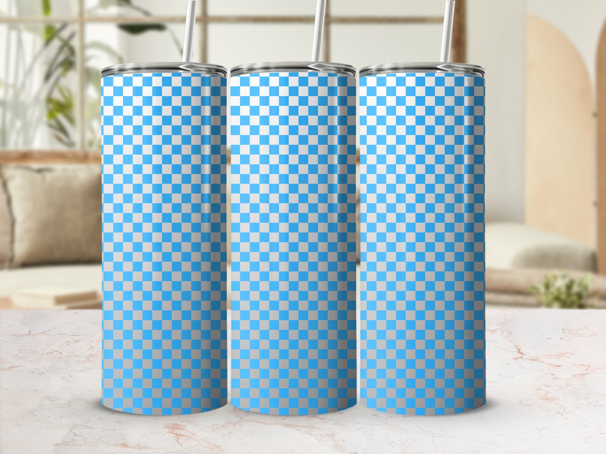 Three blue and white checkered tumblers with straws stand on a marble surface.
