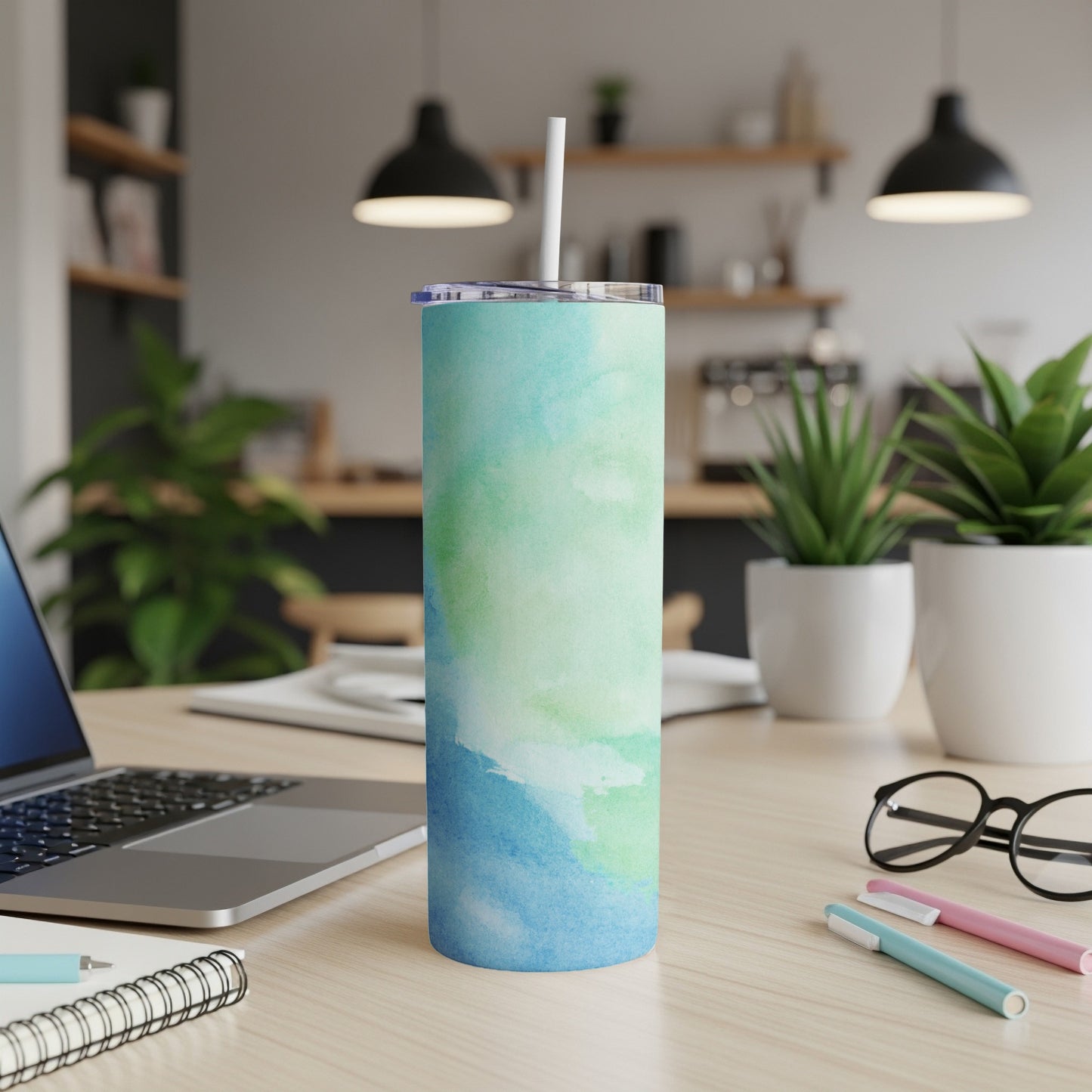 Blue and green watercolor pattern tumbler with straw on a desk.