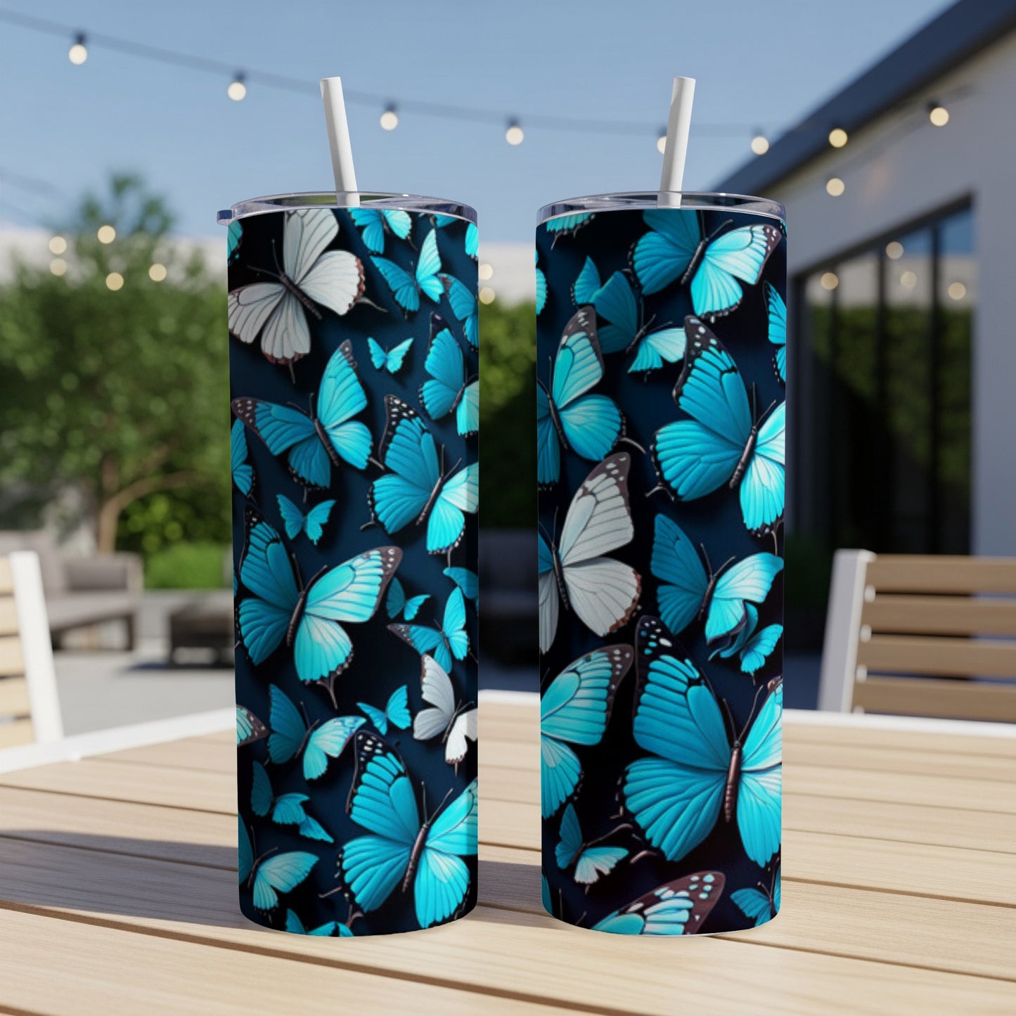 Two blue butterfly print tumblers with straws on a table outdoors.