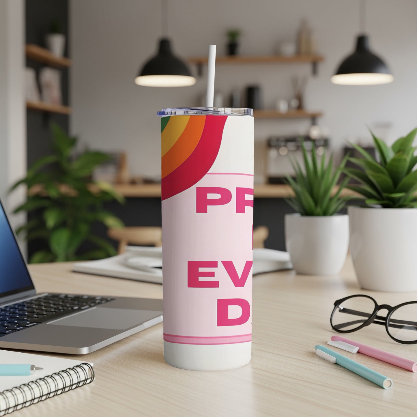 Pink tumbler with "PRIDE" and rainbow detail, on a desk with laptop and pens.