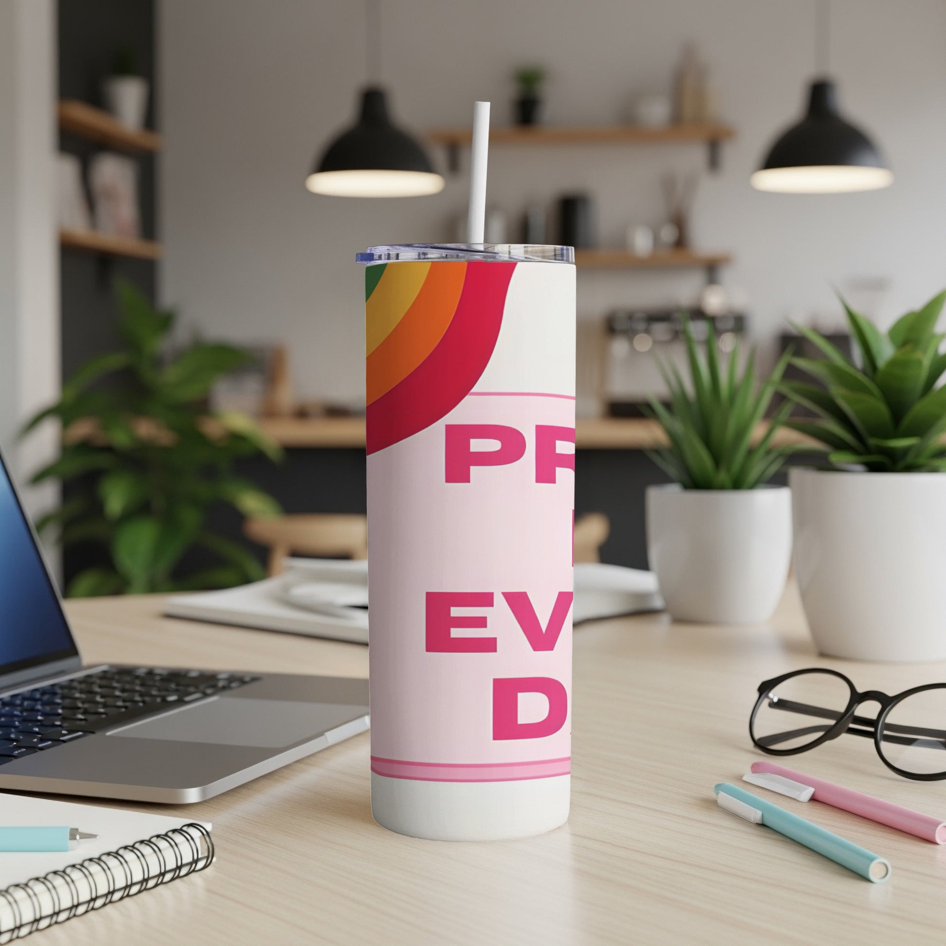 Pink tumbler with "PRIDE" and rainbow detail, on a desk with laptop and pens.