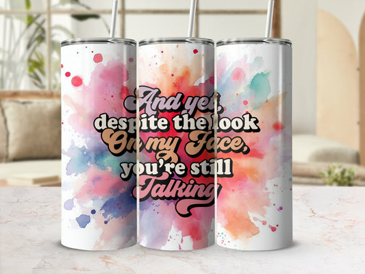 Tumbler with colorful watercolor splash and quote "And yet despite the look on my face you're still talking".