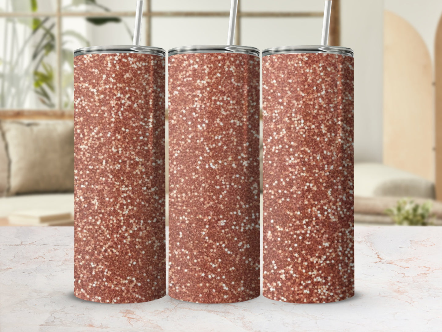Three rose gold glitter tumblers with straws on a marble countertop.