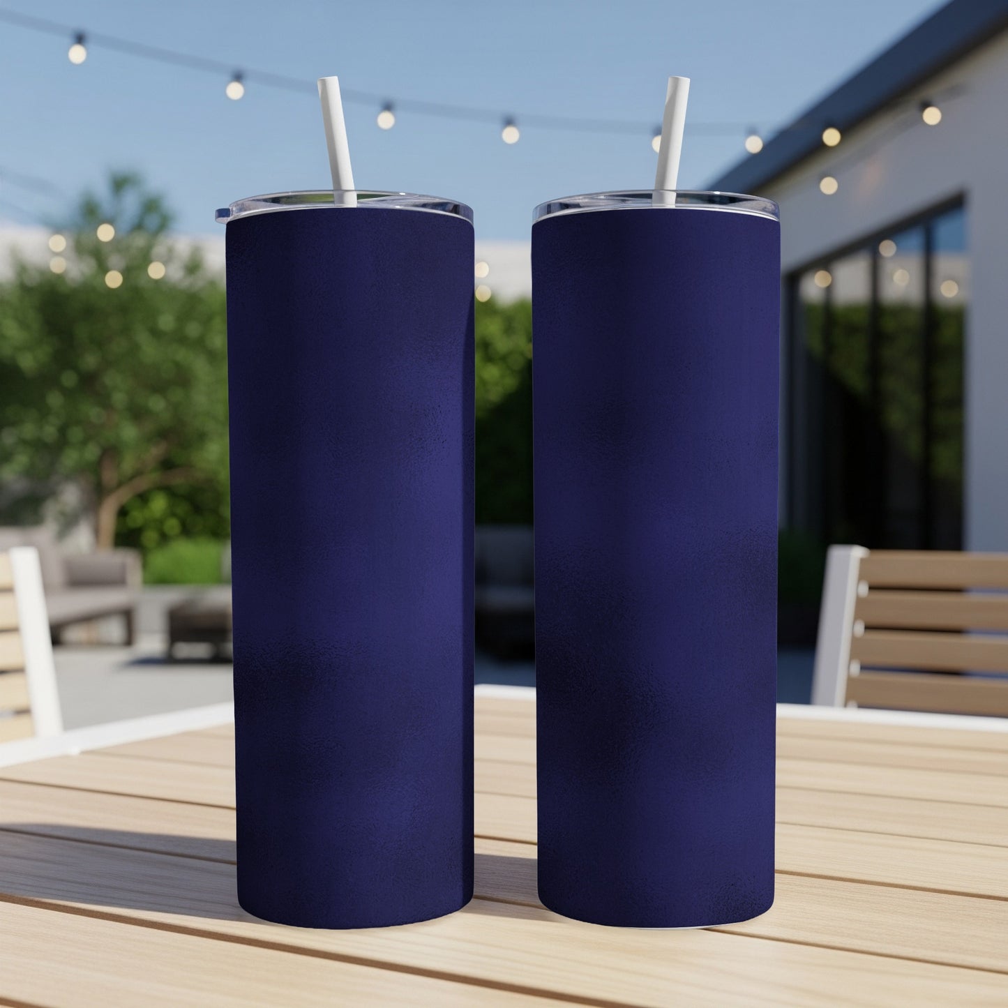 Two dark blue tumblers with white straws stand on a wooden table outdoors.