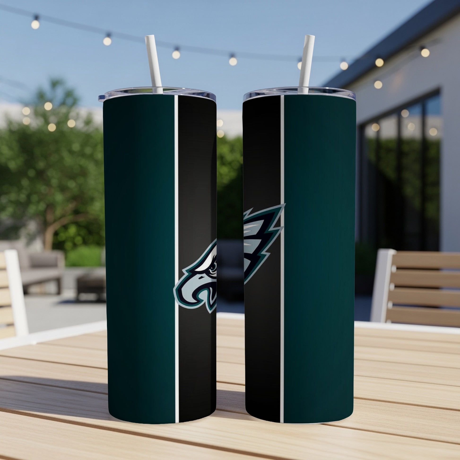 Two Philadelphia Eagles tumblers with white straws on a wooden table outdoors.