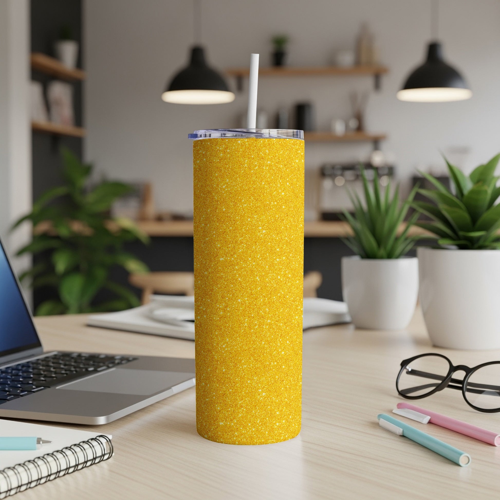 Glittery yellow tumbler with a white straw on a desk with a laptop and notebooks.