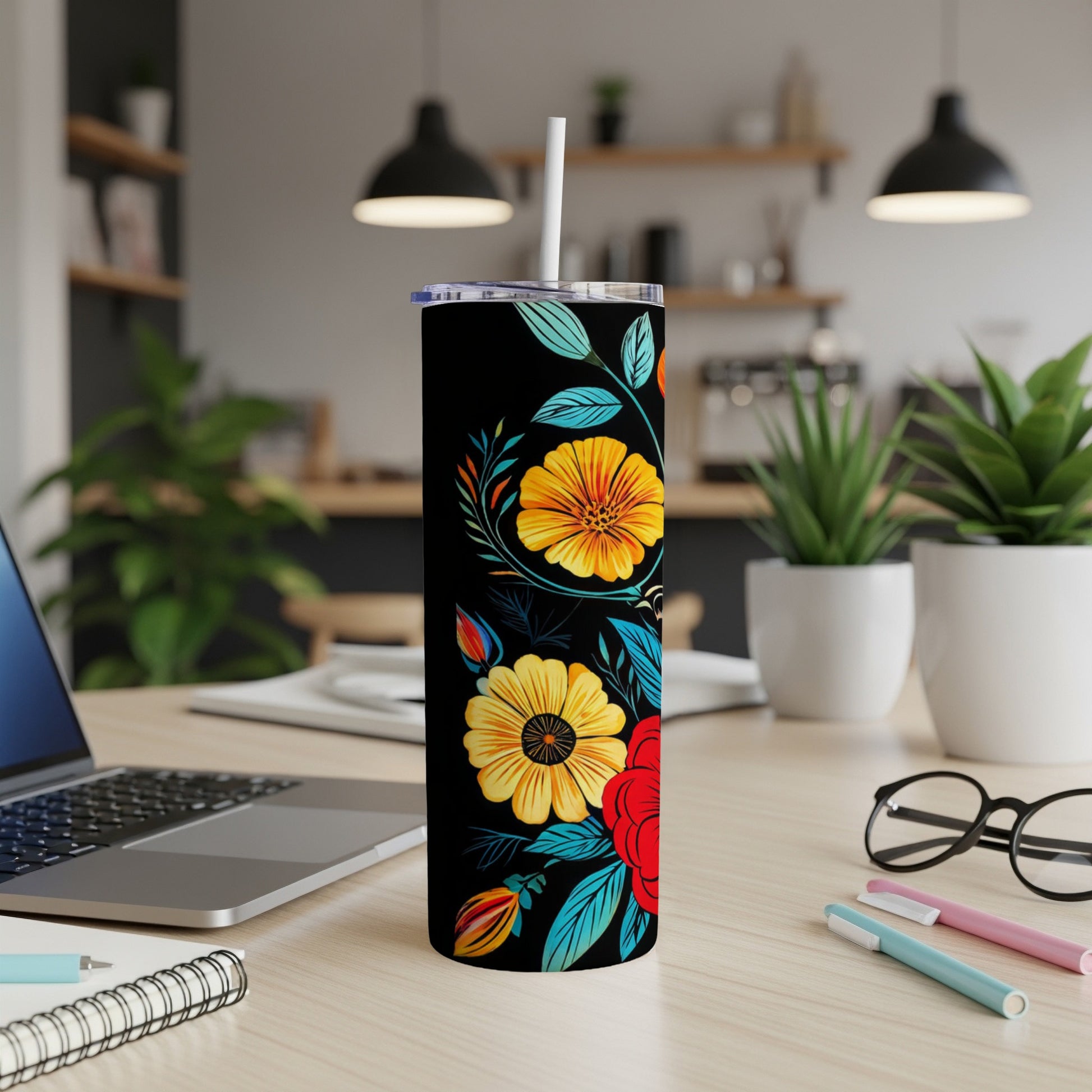 Black tumbler with colorful floral design, white straw, on a desk.