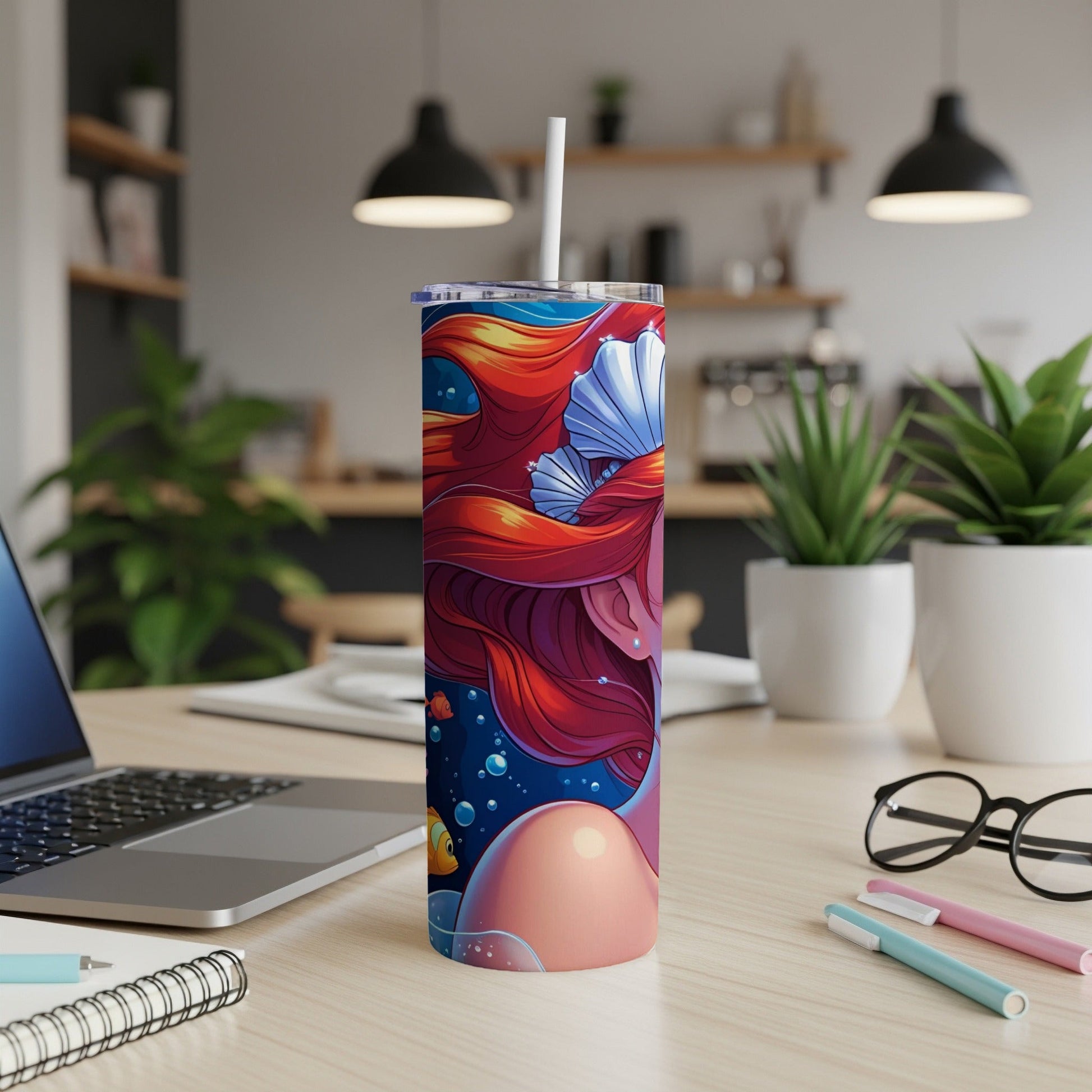 Mermaid tumbler with colorful hair, seashells, and fish on a wooden desk.