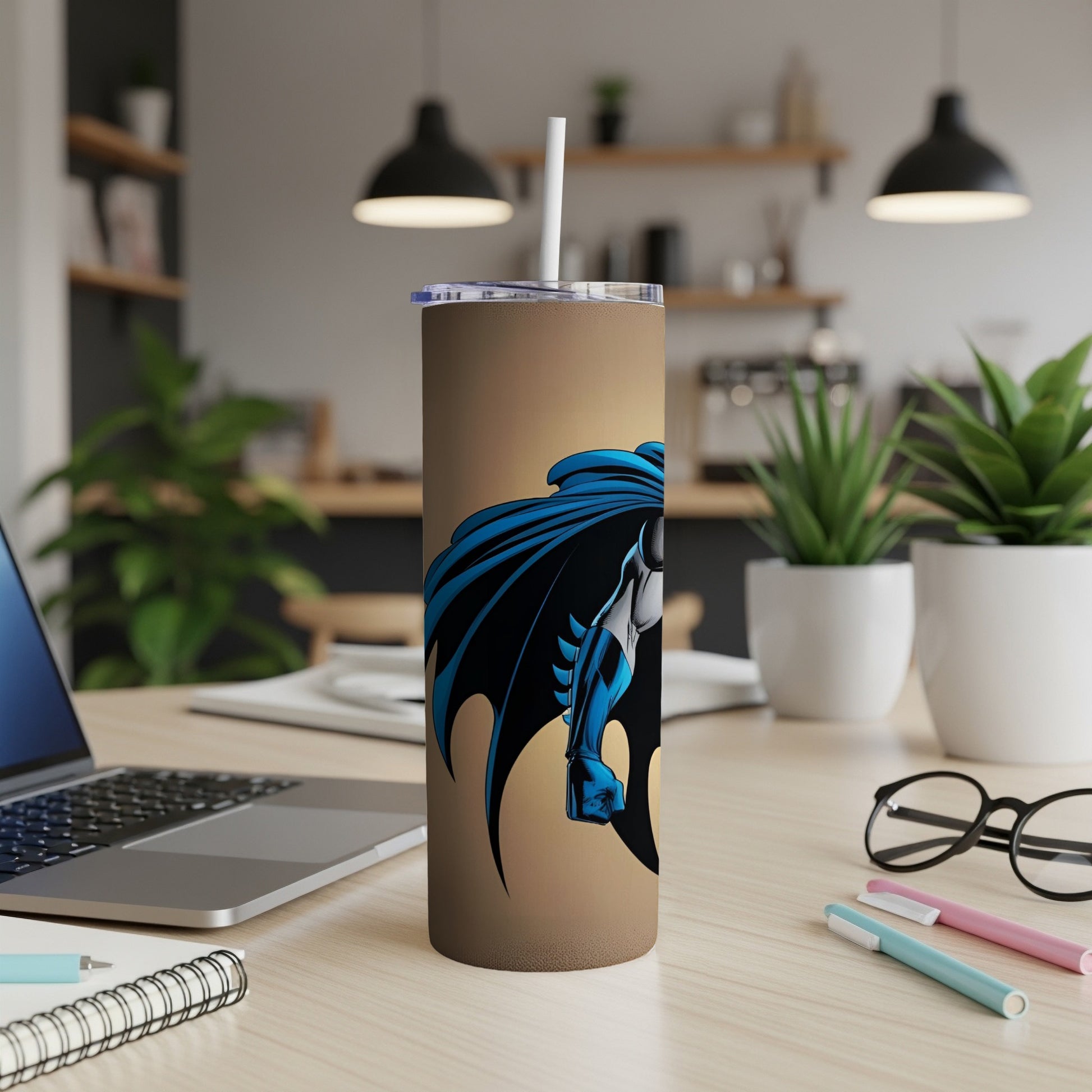 Batman tumbler with straw on desk, laptop and plants in background.