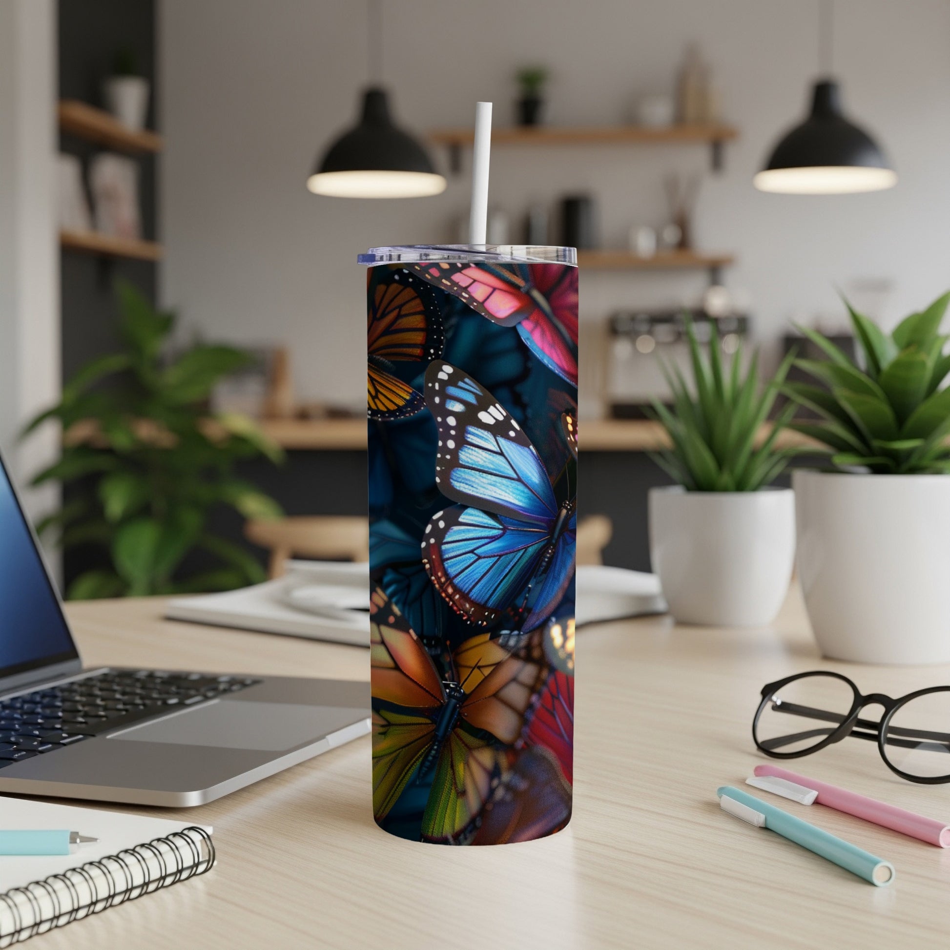 Tall tumbler with colorful butterflies on a desk with a laptop.