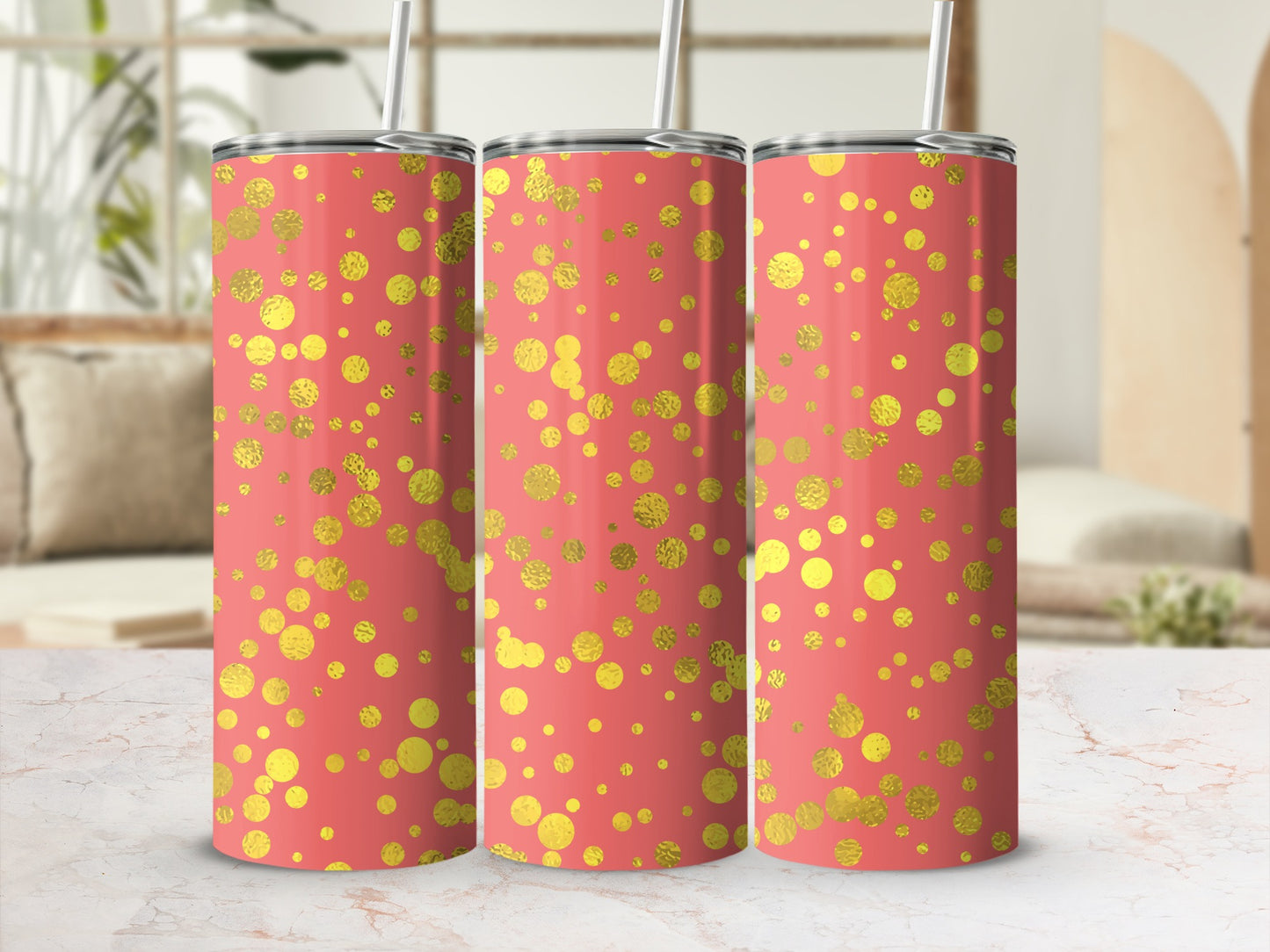 Three coral tumblers with gold glitter polka dots and straws, on a marble surface with a blurred background.