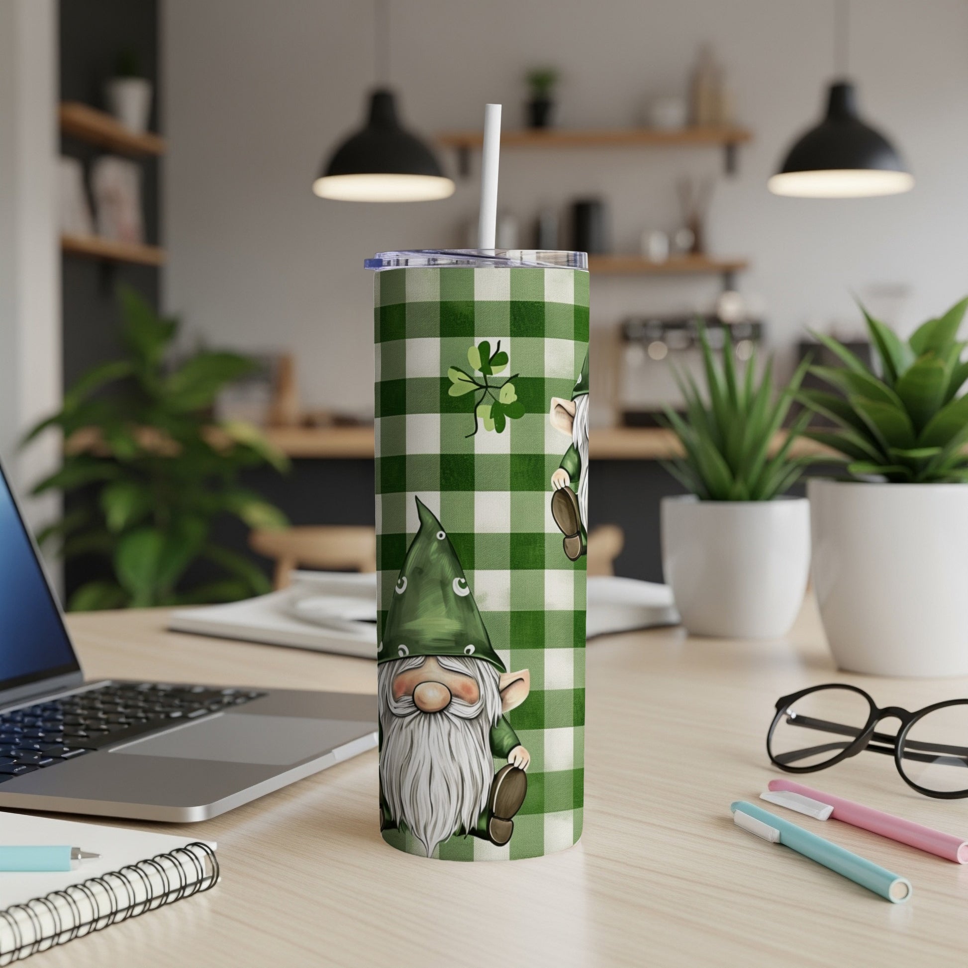 Green and white plaid tumbler with gnome design and straw on desk.