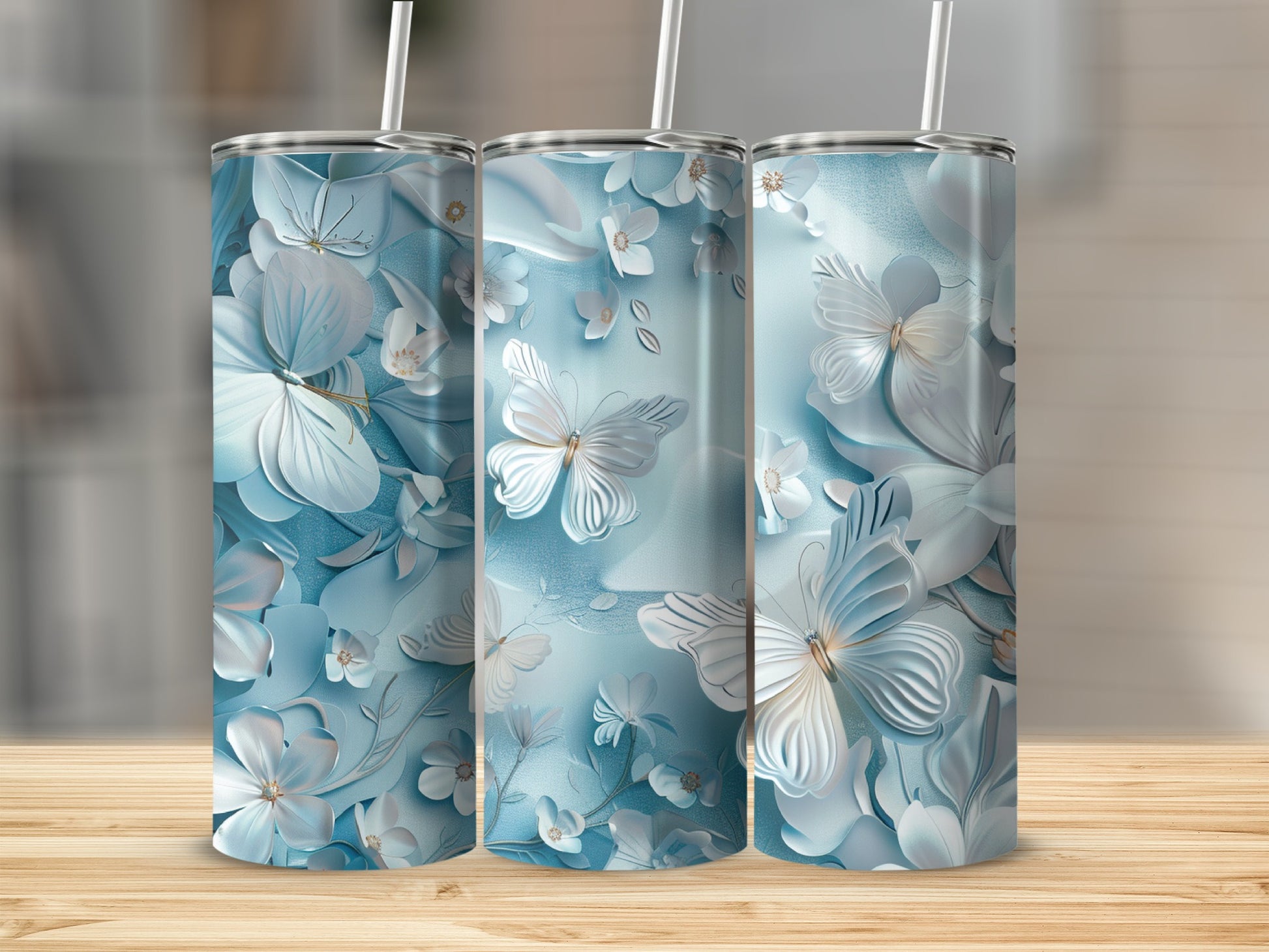 Three tall tumblers with blue floral and butterfly designs on a wooden surface.