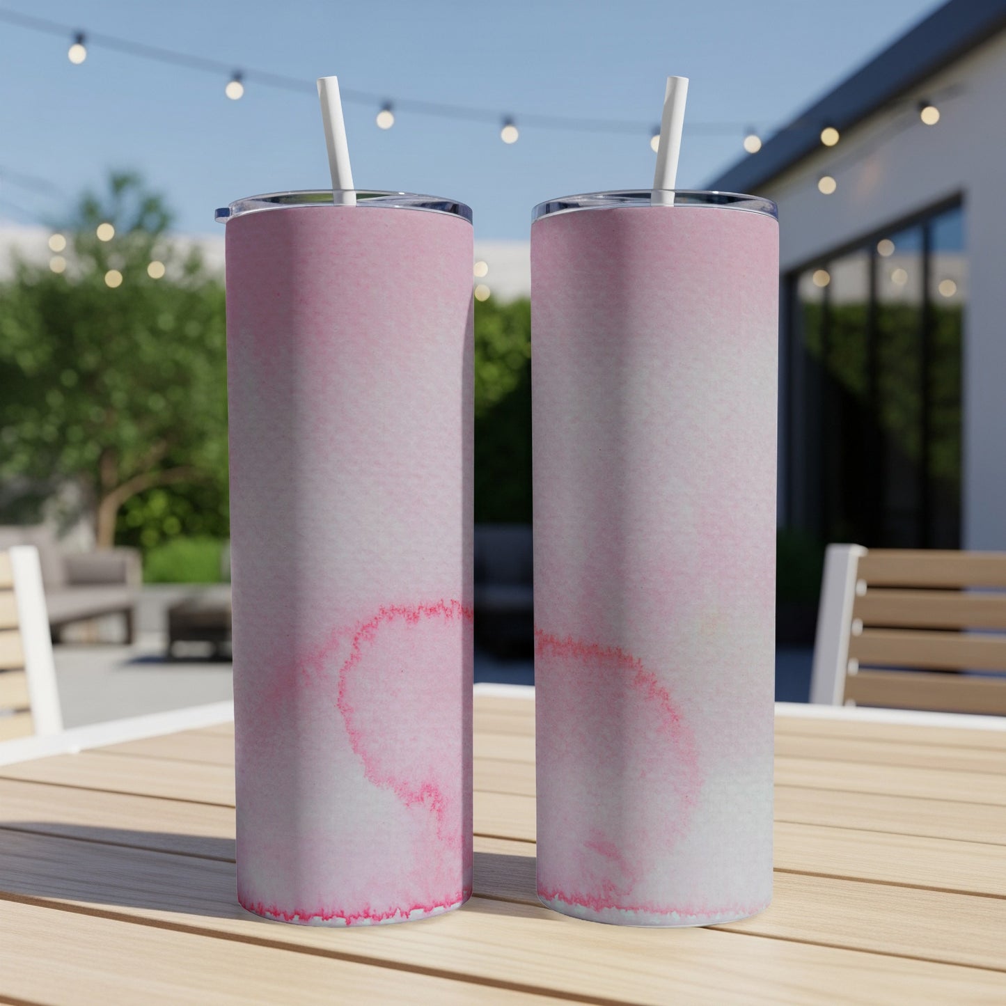 Two pink watercolor tumblers with straws on a wooden table.