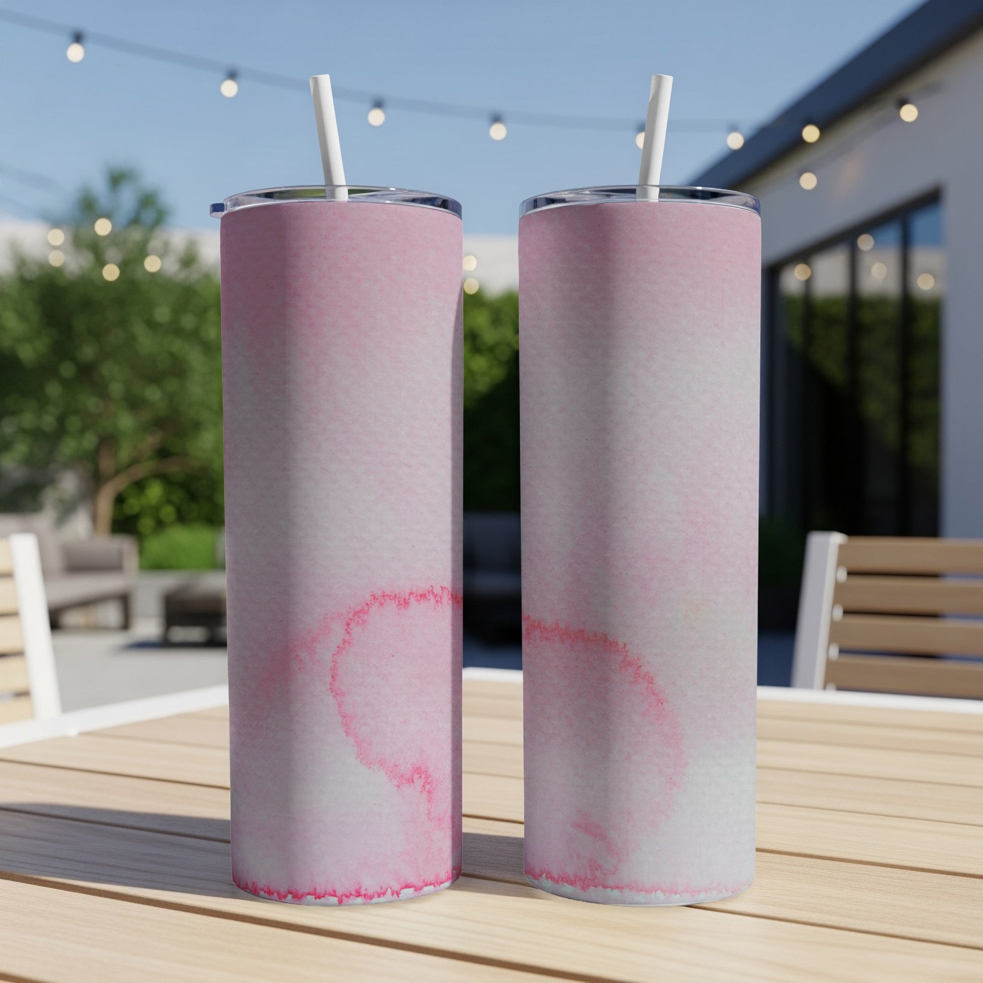 Two pink watercolor tumblers with straws on a wooden table.