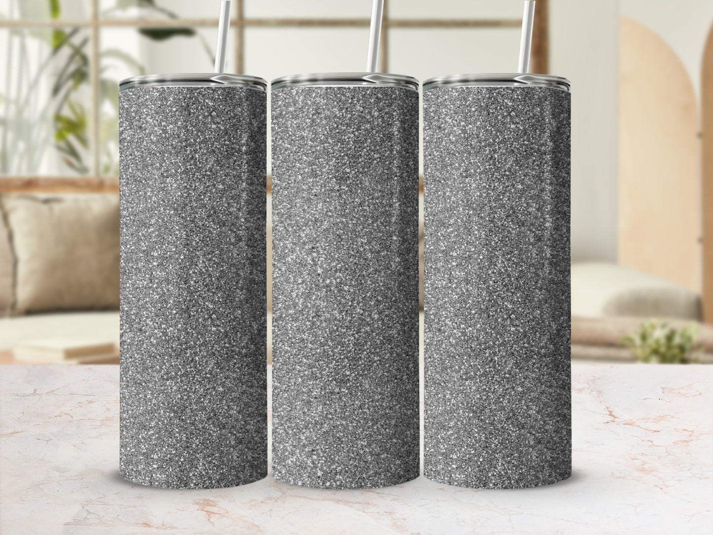 Three glittery silver tumblers with straws stand in a row.