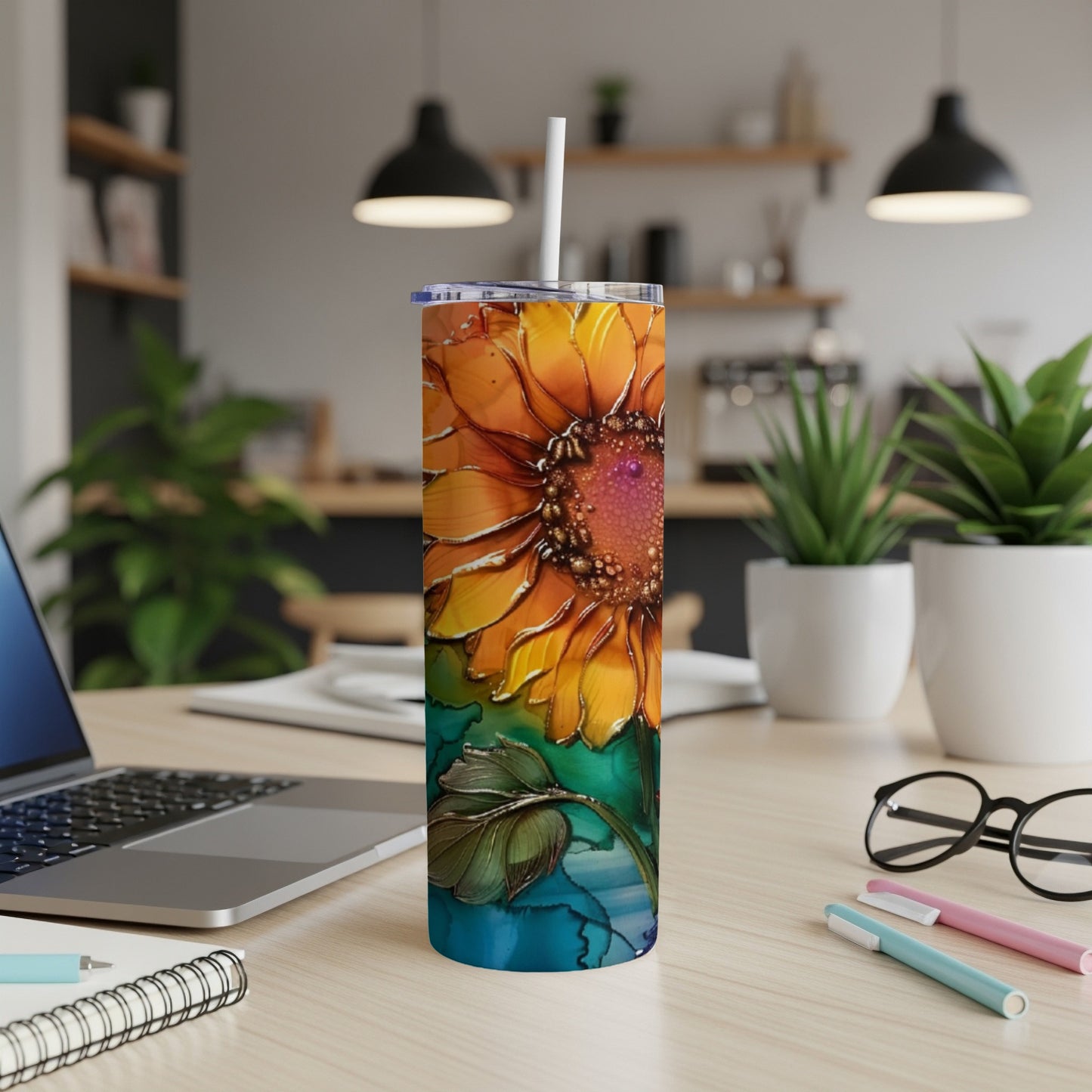Sunflower tumbler with a straw on a desk with a laptop and pens.