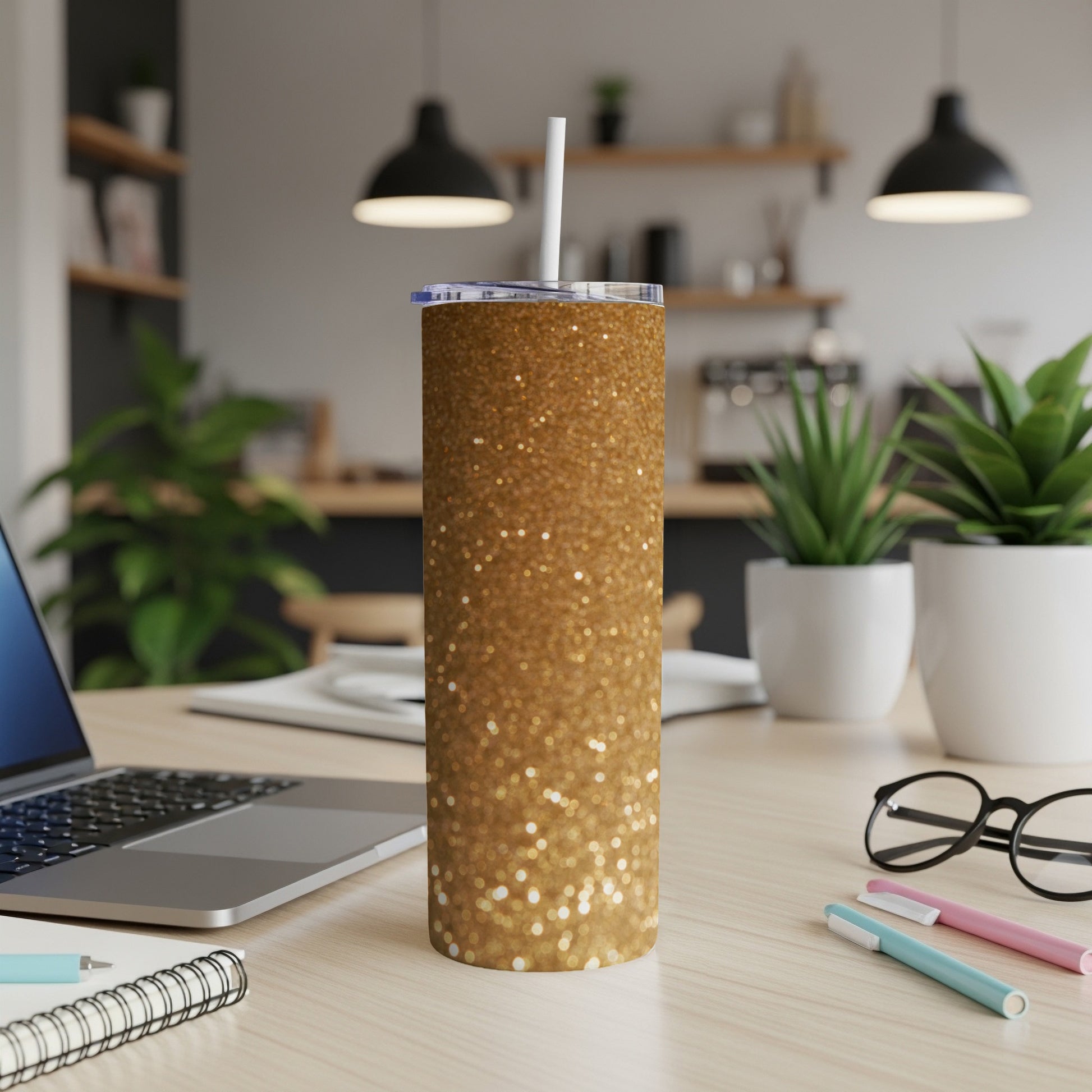 Gold glitter tumbler with straw on desk next to laptop.