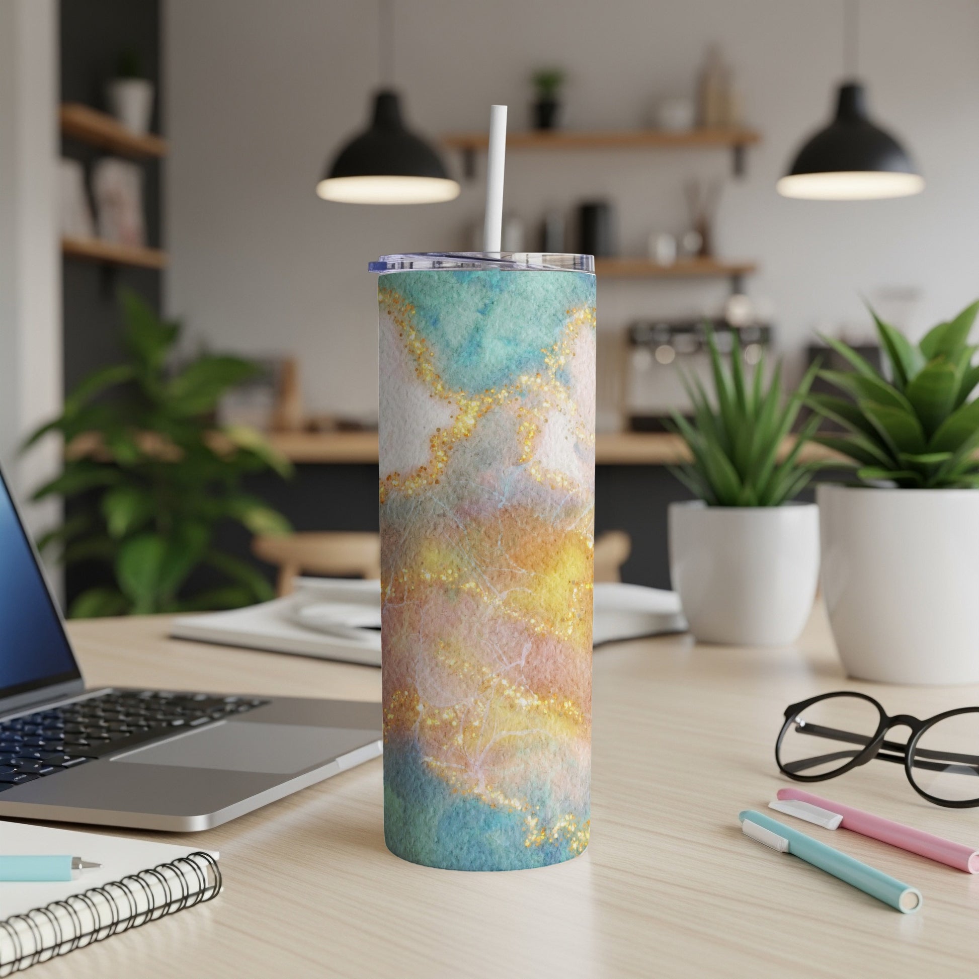 Tumbler with abstract watercolor and glitter design on desk.