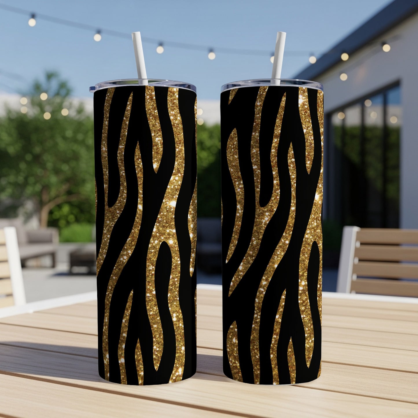 Two tumblers with black and gold glitter zebra print and white straws displayed outdoors.