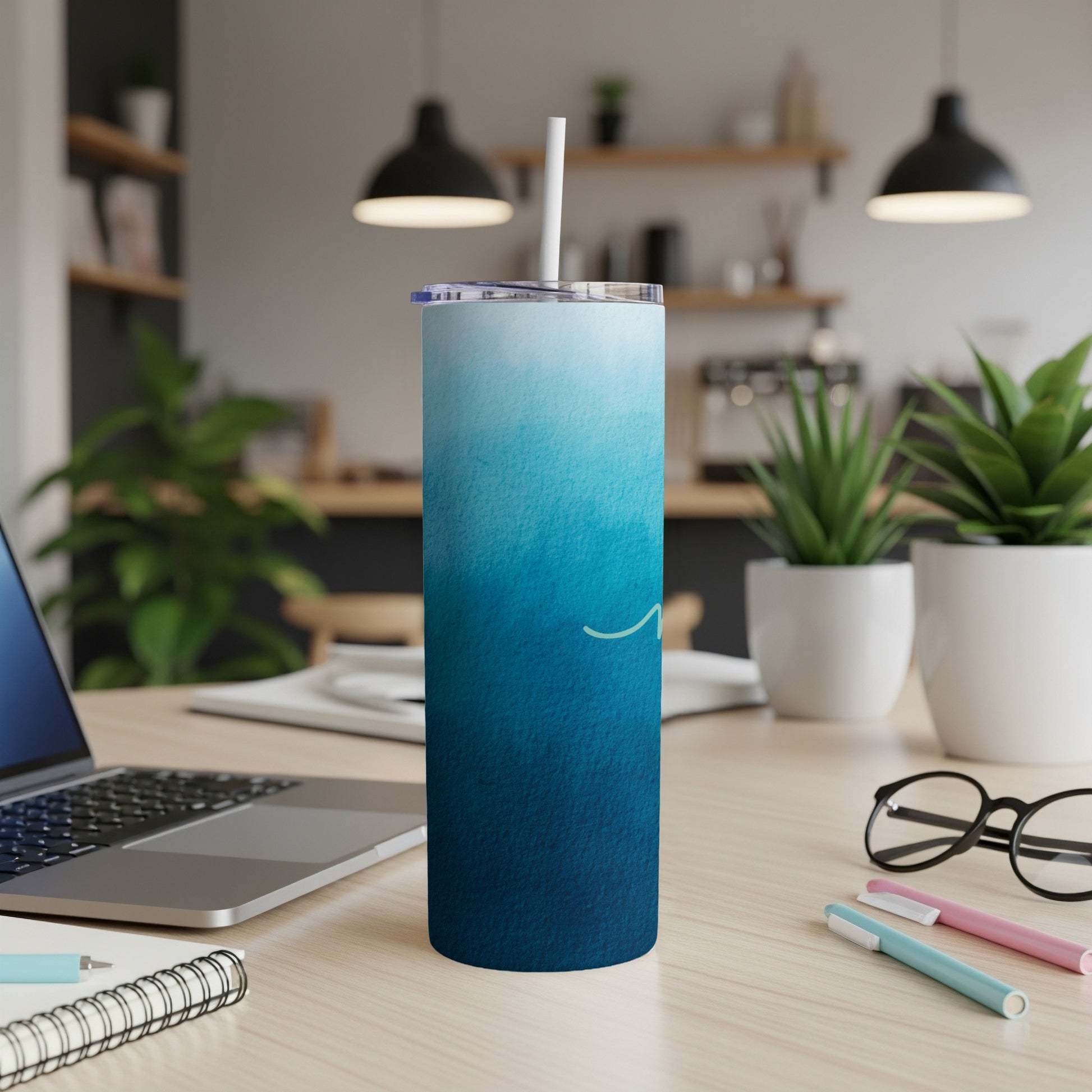 Blue ombre tumbler with straw on desk next to laptop and pens.