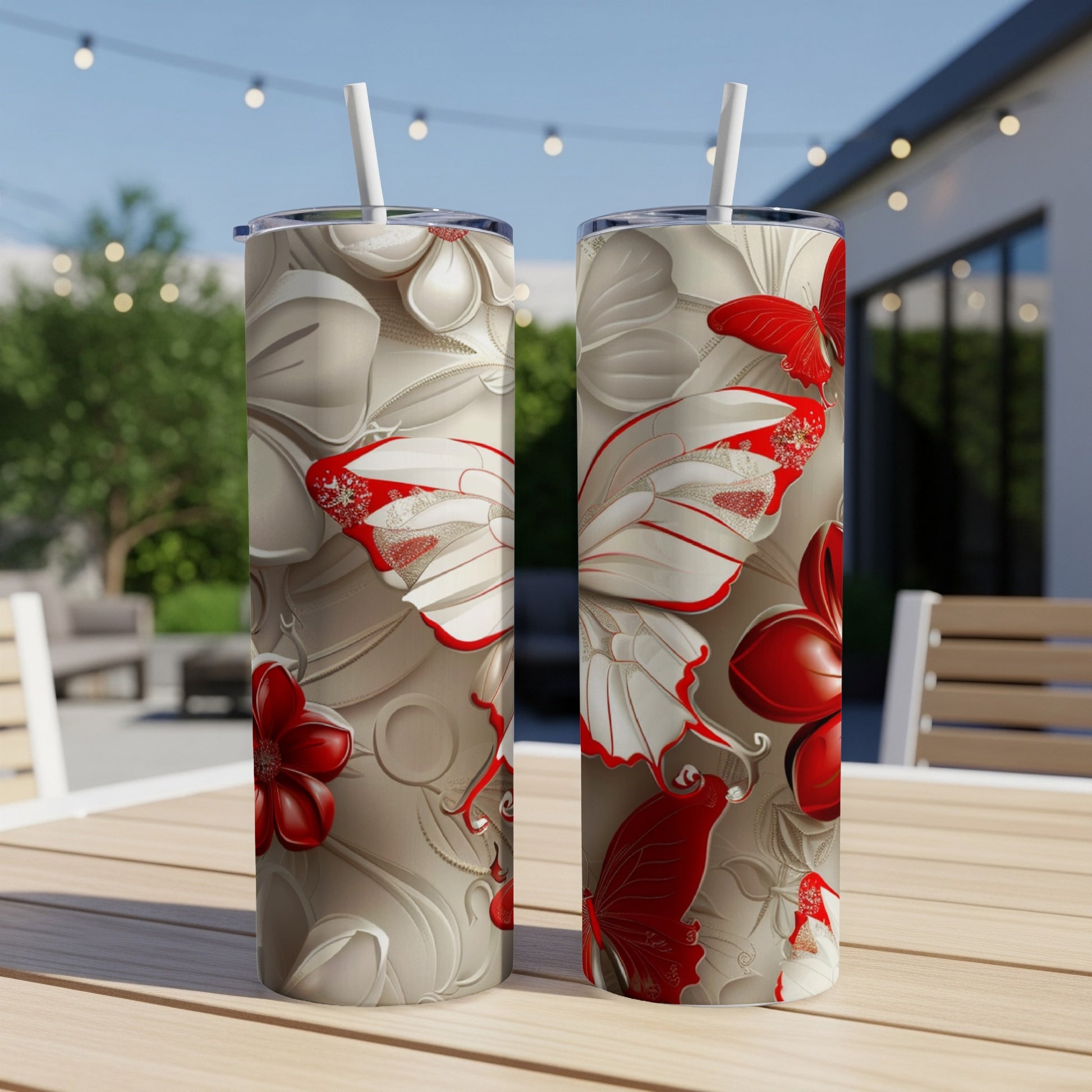 Two tumblers with red and white floral and butterfly designs on a patio table.