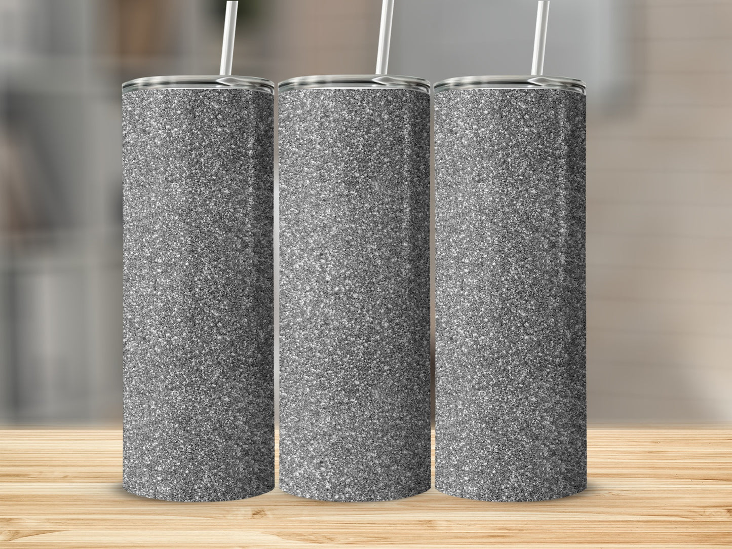Three silver glitter tumblers with straws stand on a wooden surface.