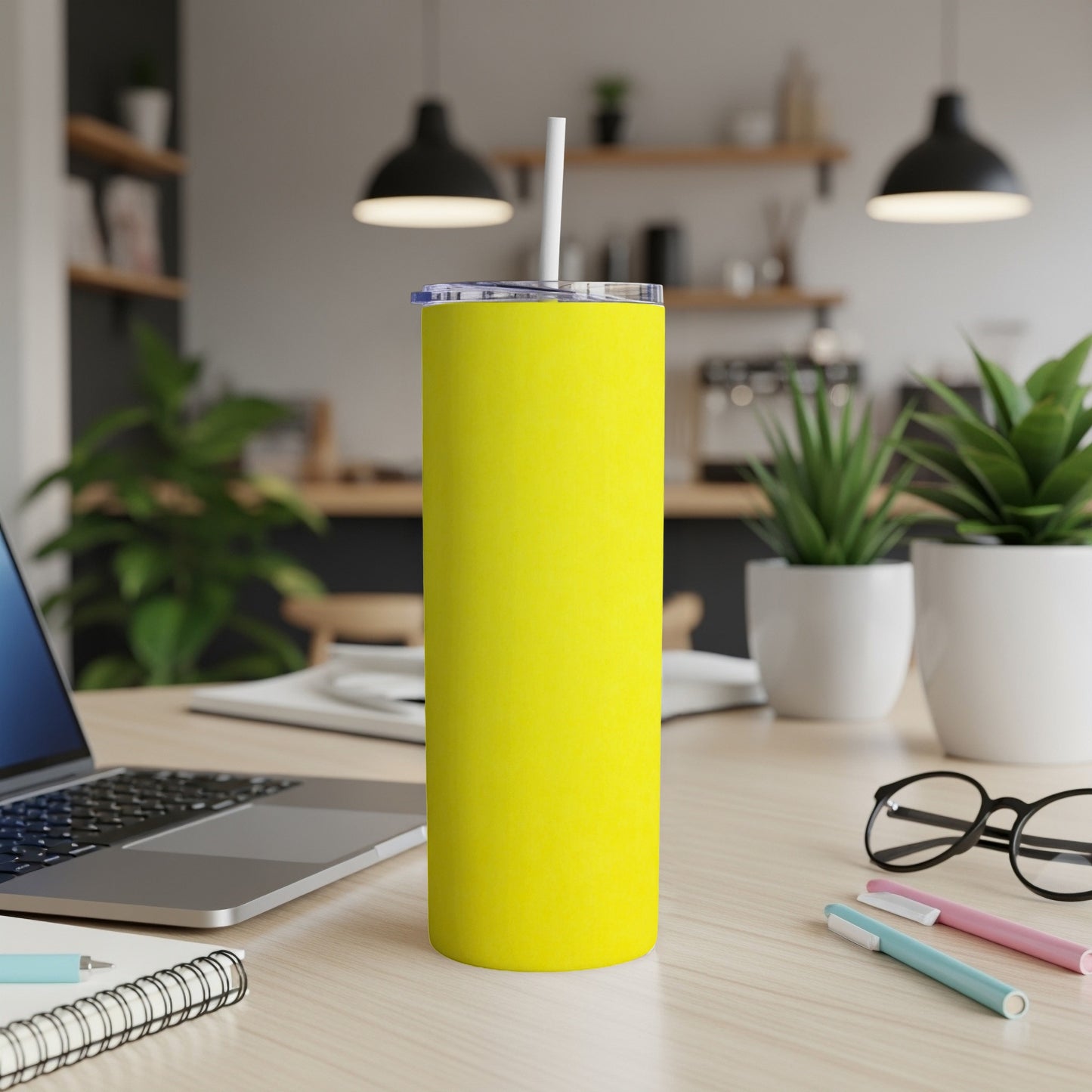 Bright yellow tumbler with straw on a desk next to a laptop.