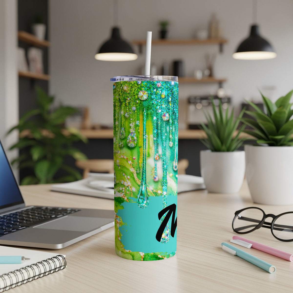 Green and blue glittery tumbler with dripping effect and black letter M.