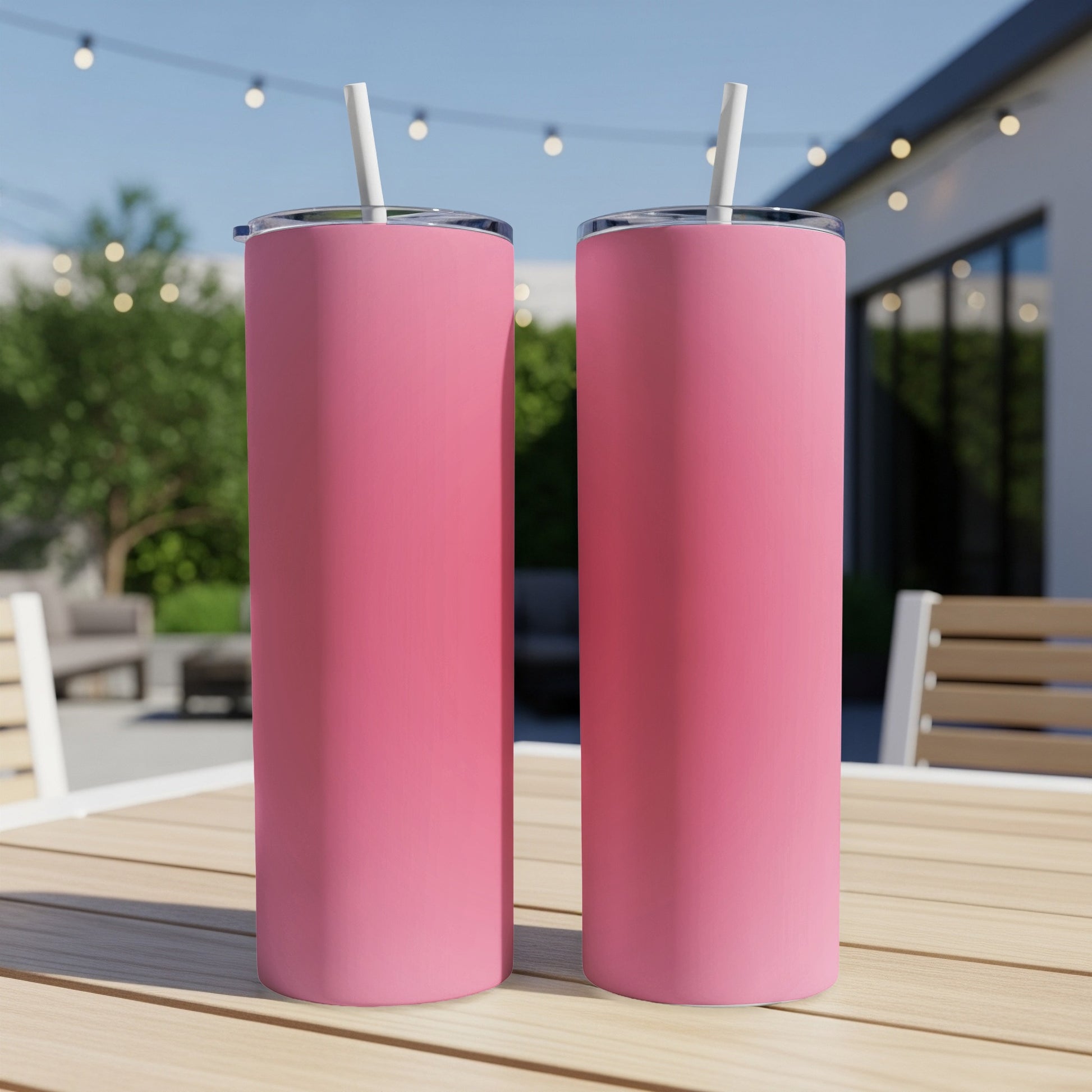 Two pink tumblers with straws on a wooden table outdoors.