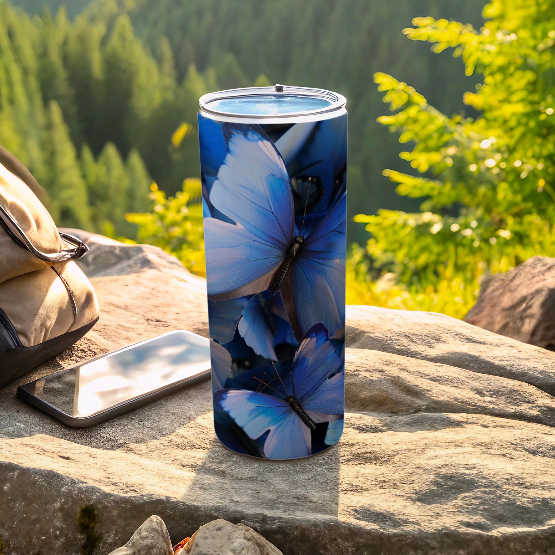 Blue butterfly pattern on a stainless steel tumbler with phone and backpack outdoors.