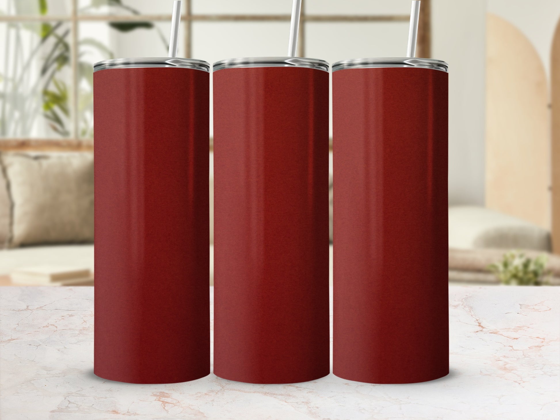 Three tall, plain red tumblers with straws on a marble surface.