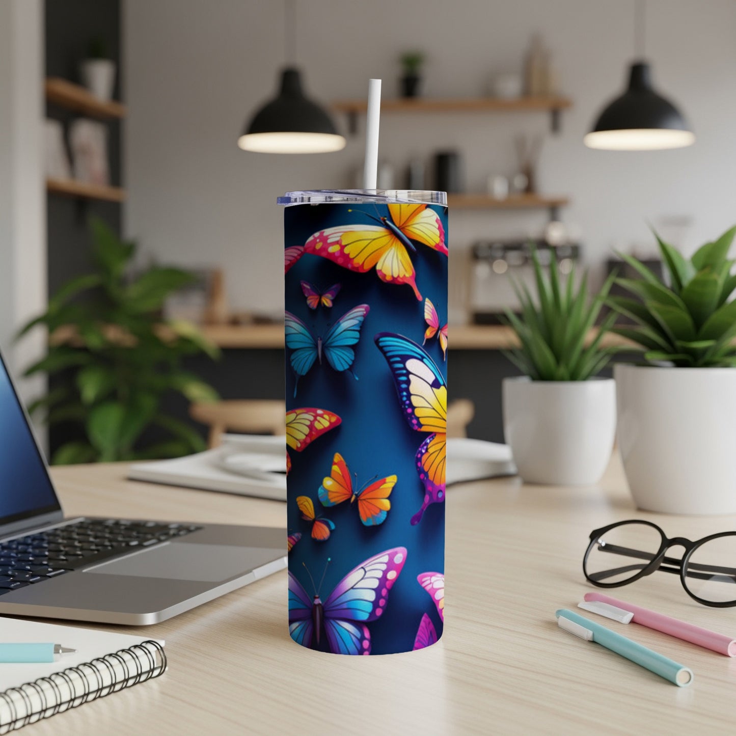 Blue tumbler with colorful butterflies and a straw on a desk.