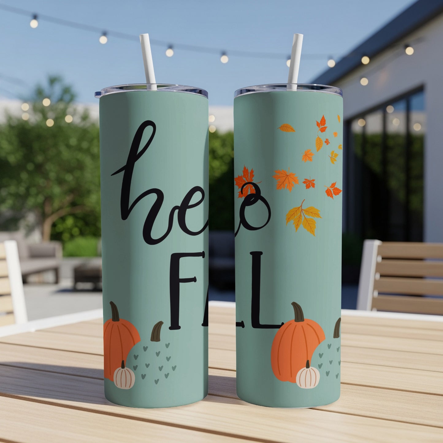 Two teal tumblers with "hello fall" and pumpkin illustrations on a table.