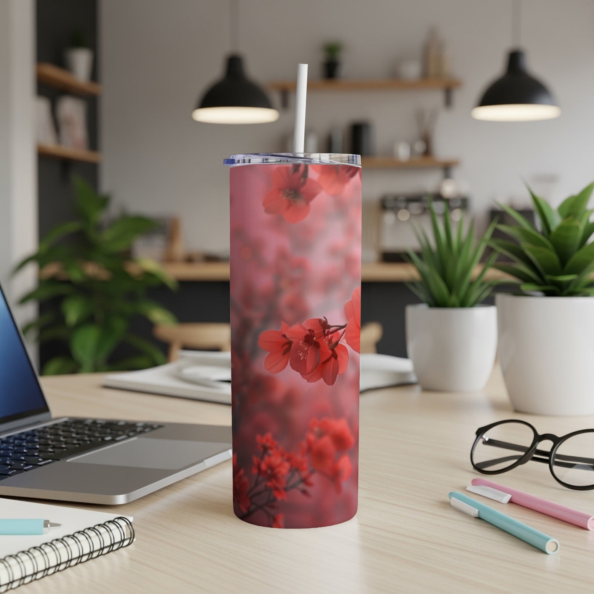 Red floral design on a stainless steel tumbler with a straw, on a desk.