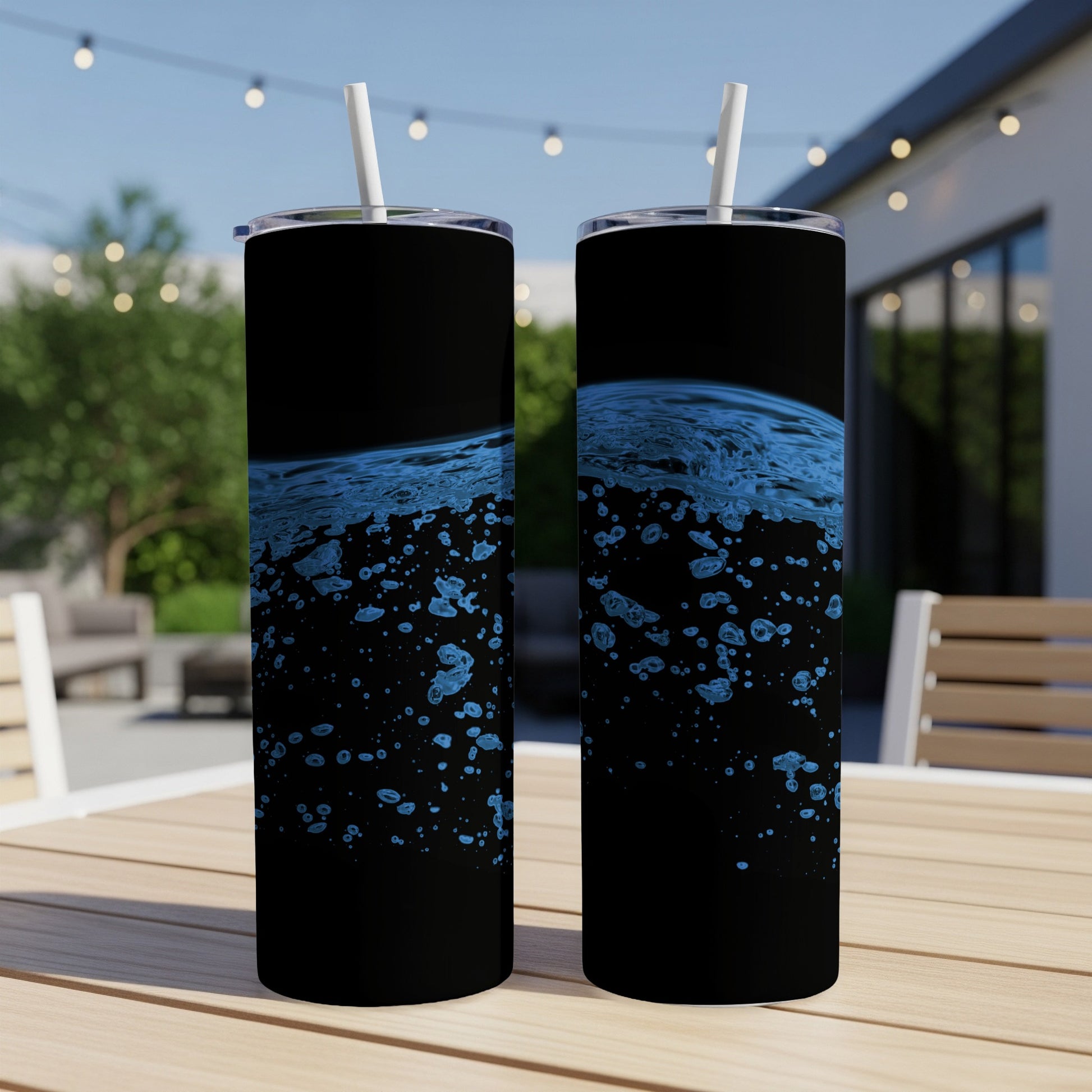 Two black tumblers with splashing blue water design on an outdoor table.