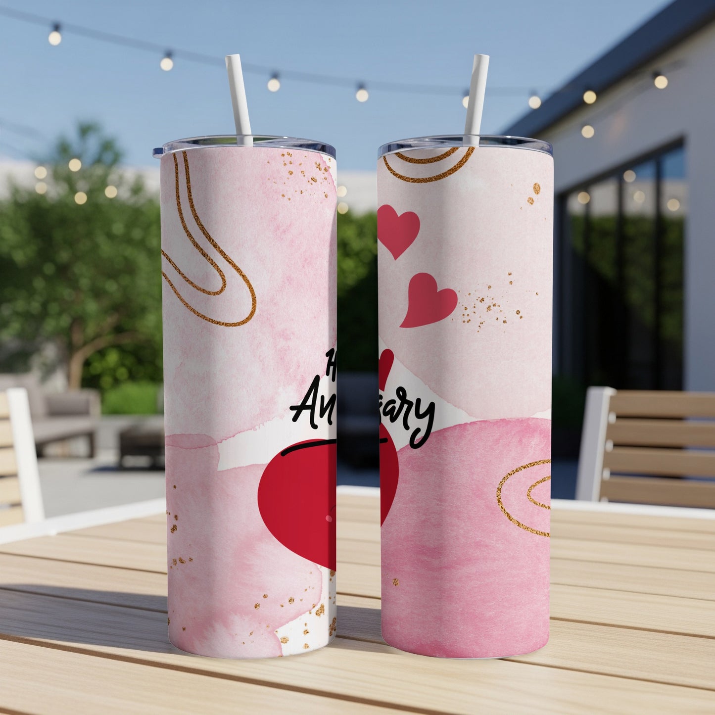 Two pink tumblers with "Happy Anniversary" and hearts, on a table outdoors.
