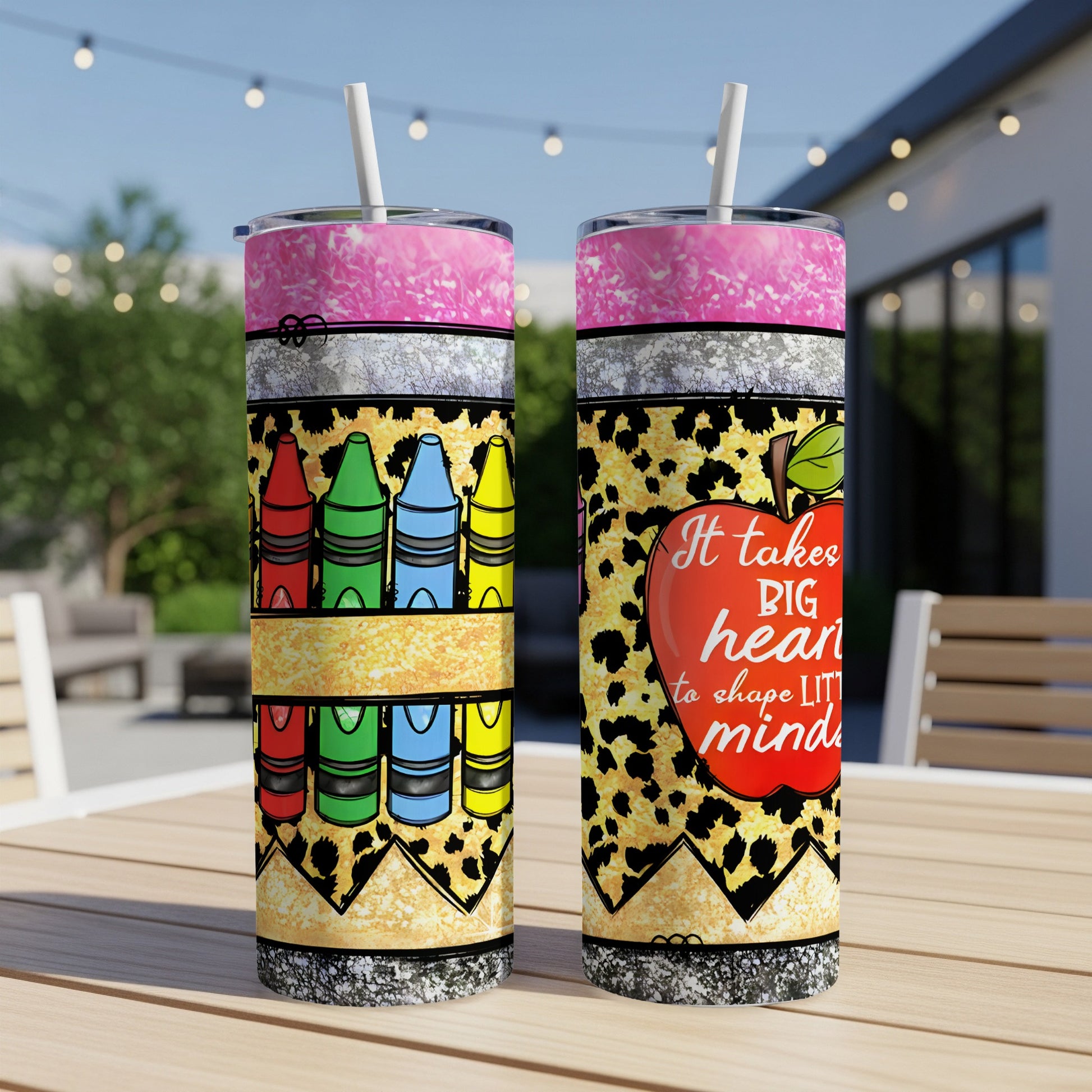 Two tumblers with colorful crayons and a red apple on a wooden table.