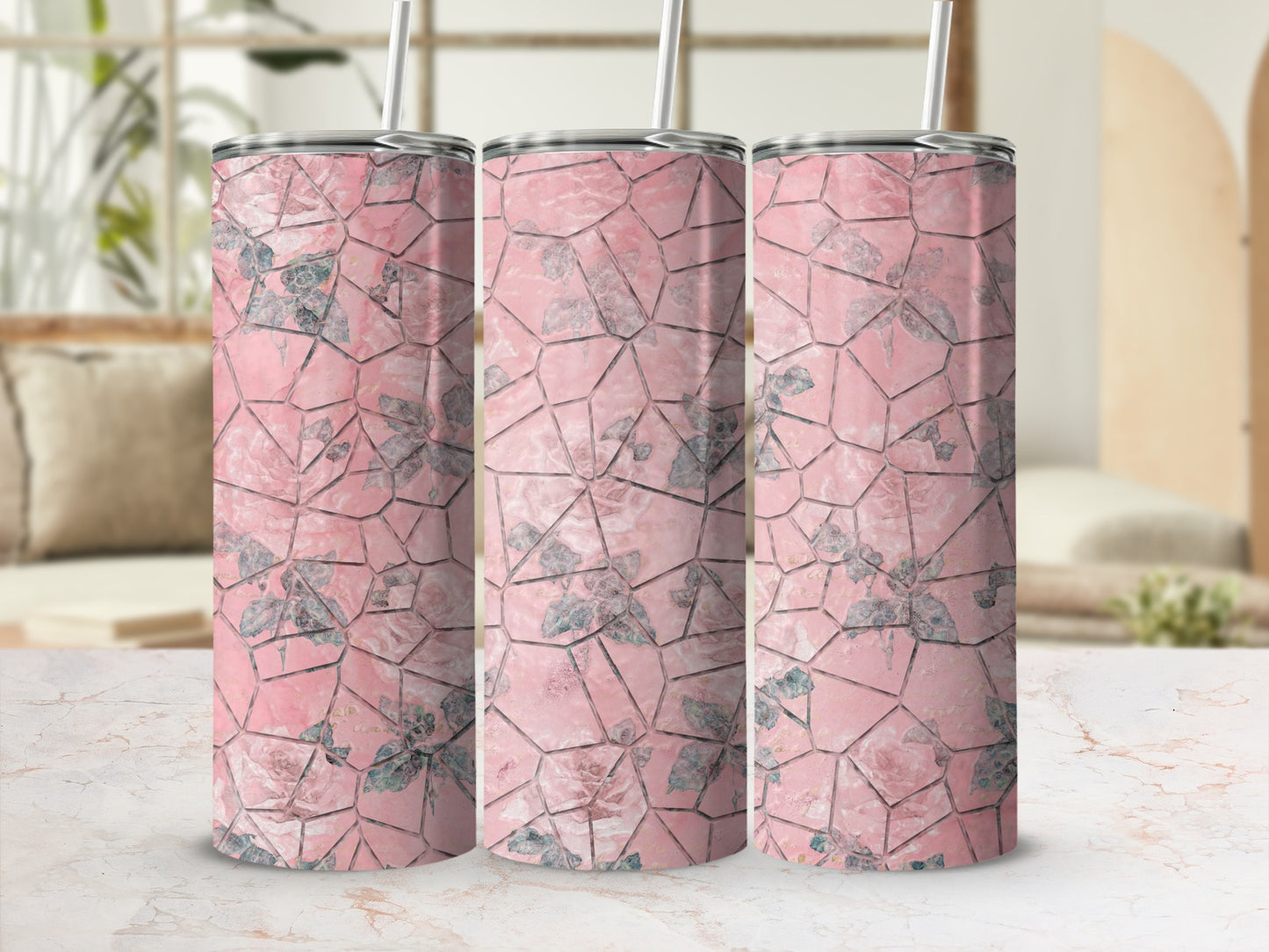 Three pink floral patterned tumblers with straws on a marble surface.