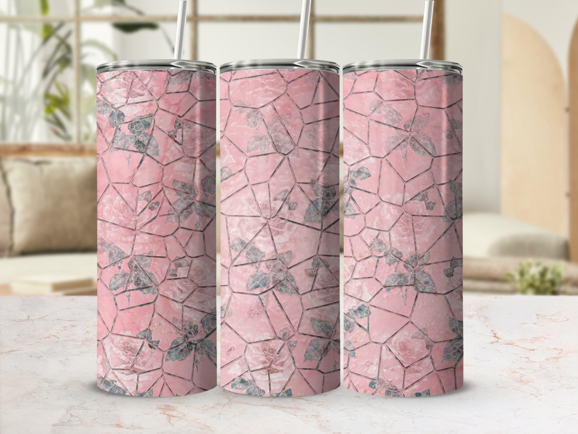 Three pink floral patterned tumblers with straws on a marble surface.