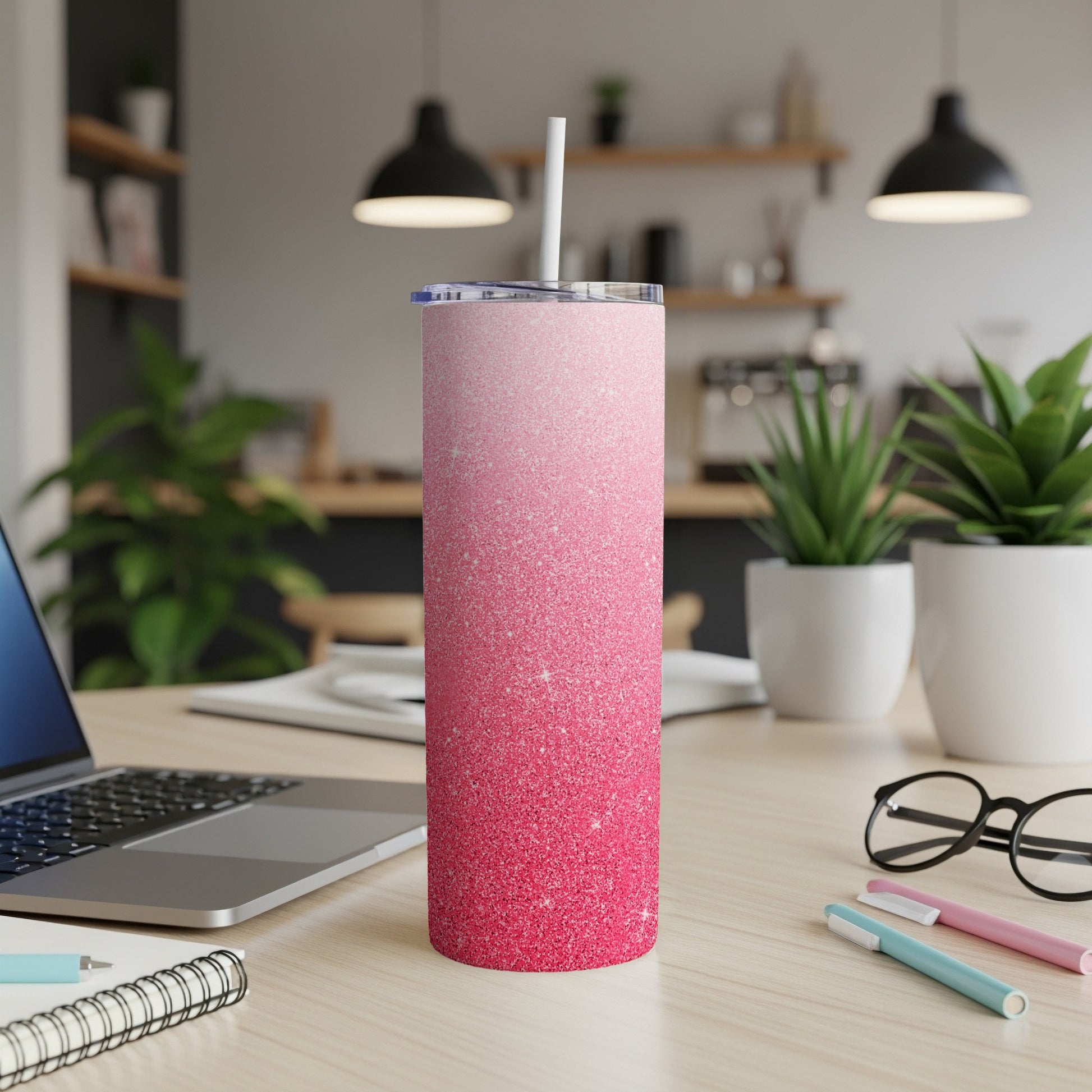 Pink glitter skinny tumbler with straw on a desk with a laptop and pens.
