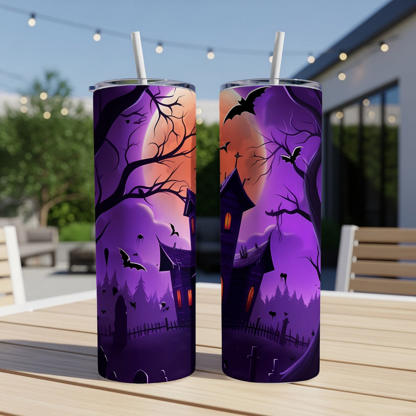 Two tumblers with Halloween haunted house and bat designs on an outdoor table.
