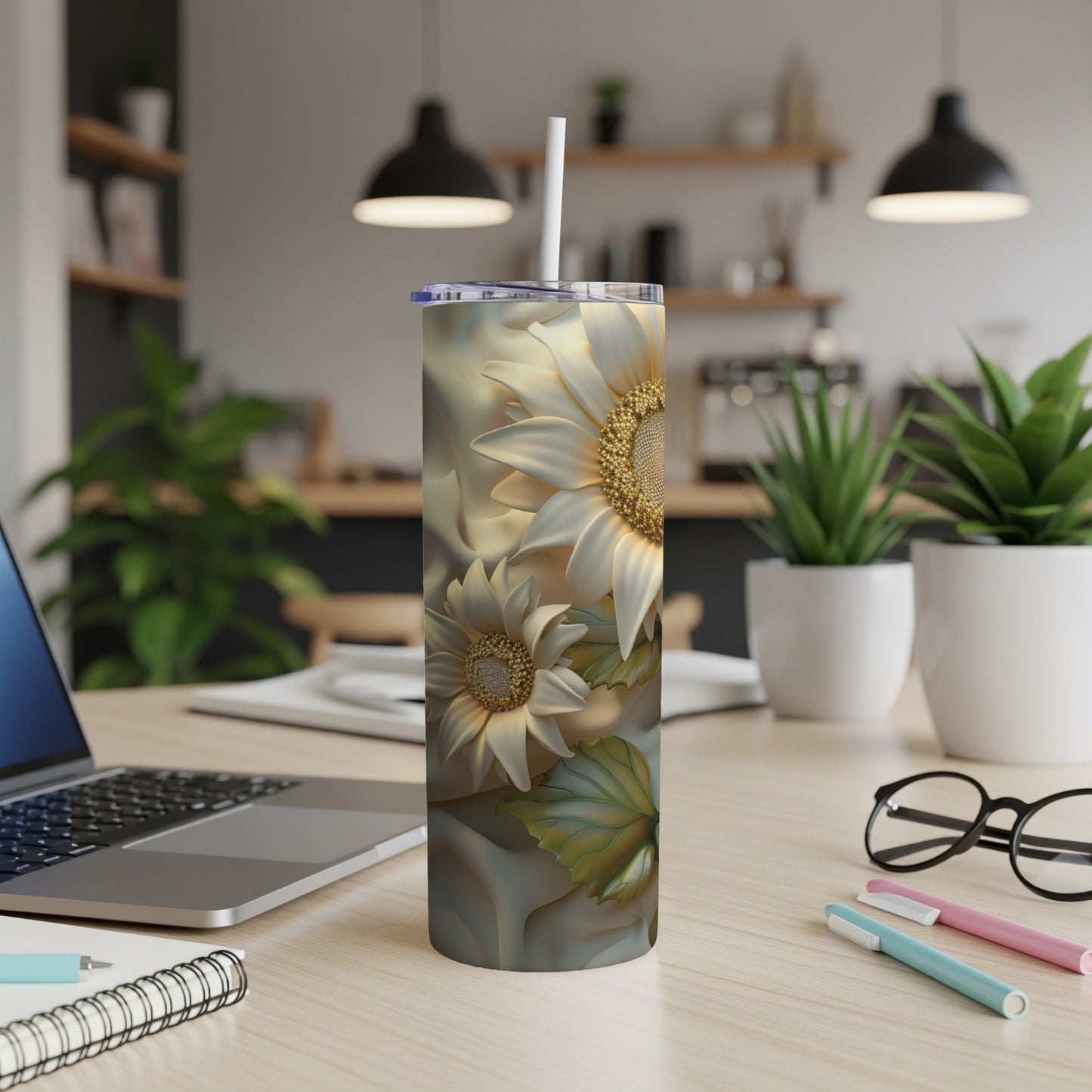 Sunflower tumbler with straw on a desk with a laptop and pens.