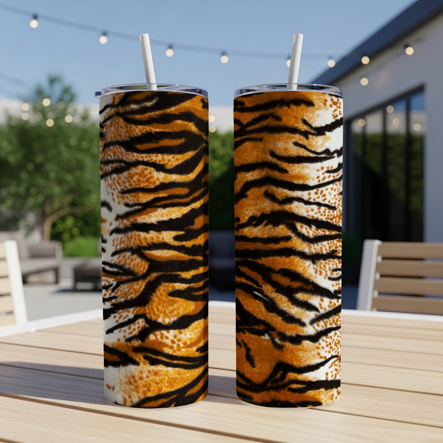 Two tumblers with tiger stripe patterns and white straws on a wooden table.